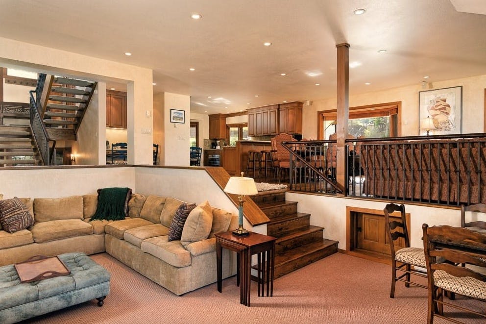 Inside the living room of Residence 5 at Woodrun V Snowmass, showcasing a wrap-around couch, chairs, kitchen, and stairs up to the bedrooms