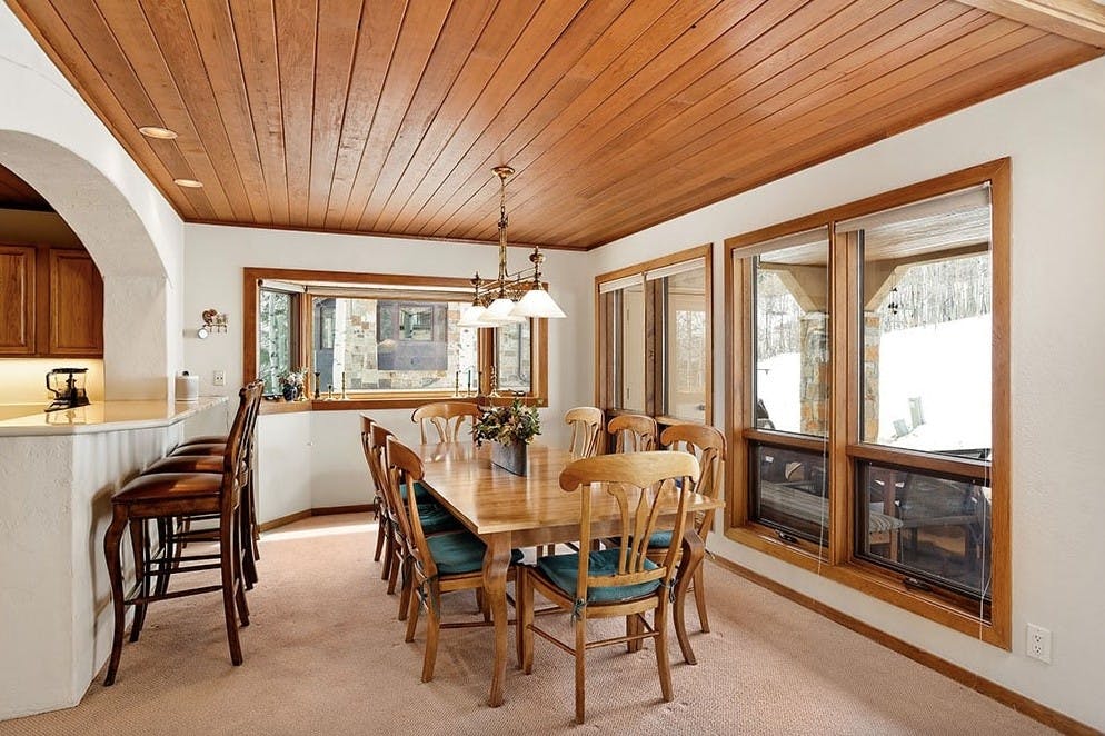 The modern sleek cabin-feel dining room with a wooden ceiling and wooden tables, plus huge windows with views of the slopes at Snowmass inside Residence 17 at Woodrun V