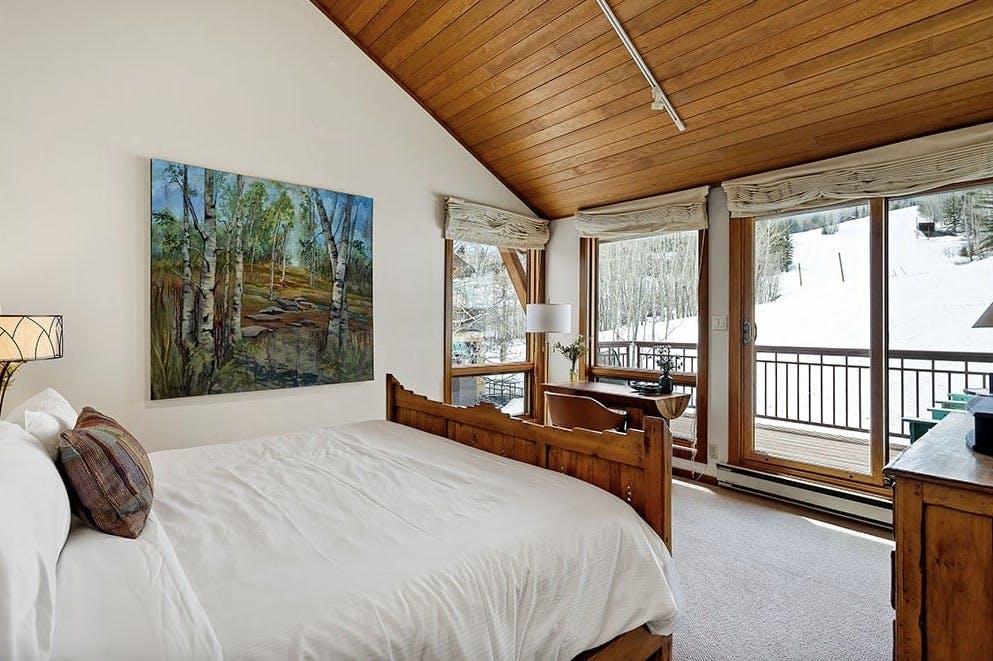 A bedroom inside Residence 17 at Woodrun V Snowmass with a big king bed with a white comforter, and huge windows with views of the Snowmass ski resort