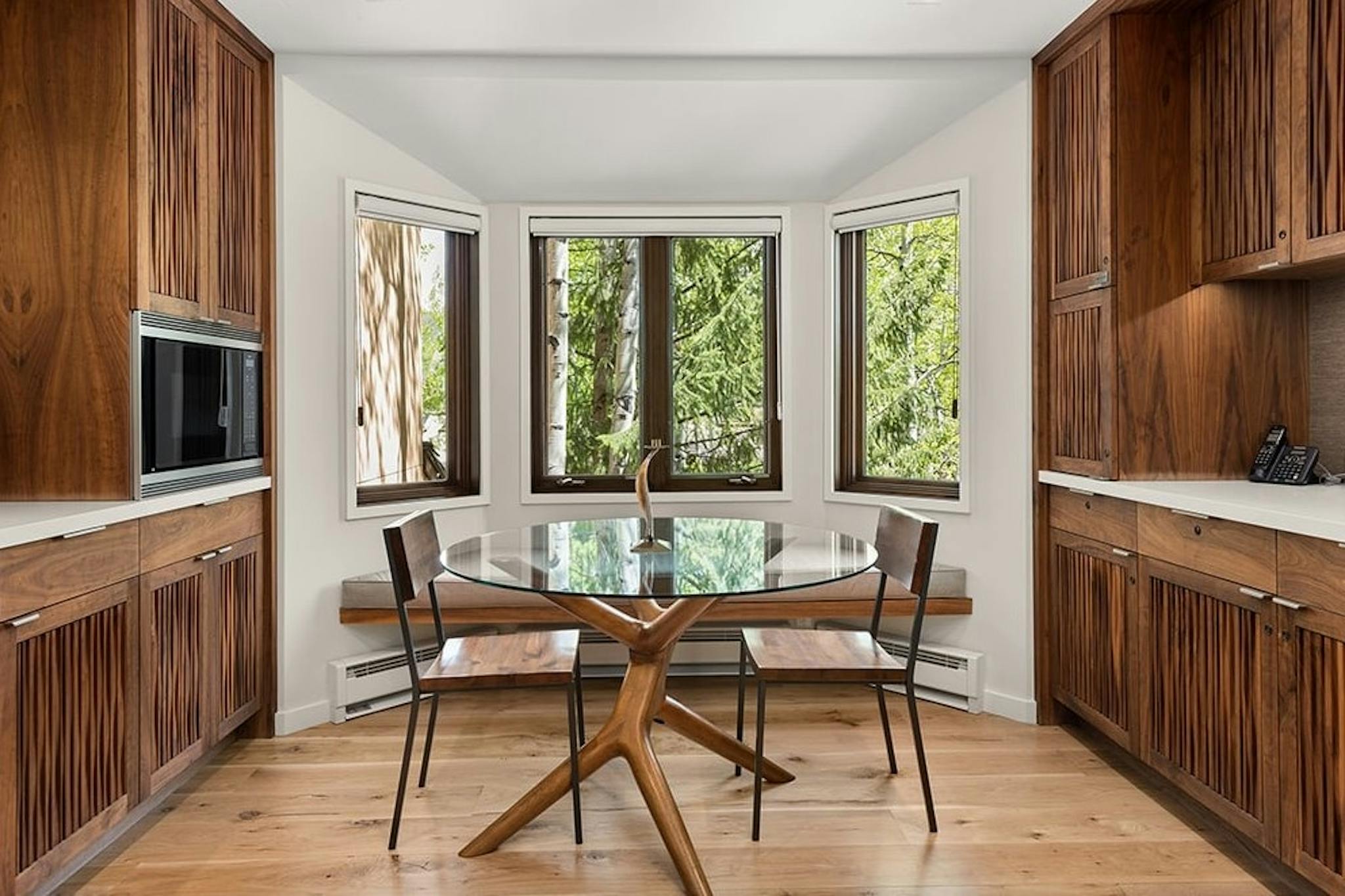 Sleek dining room of Residence 16 at Woodrun V Snowmass with wooden cabinets, beautiful forest views, and a modern glass dining room table