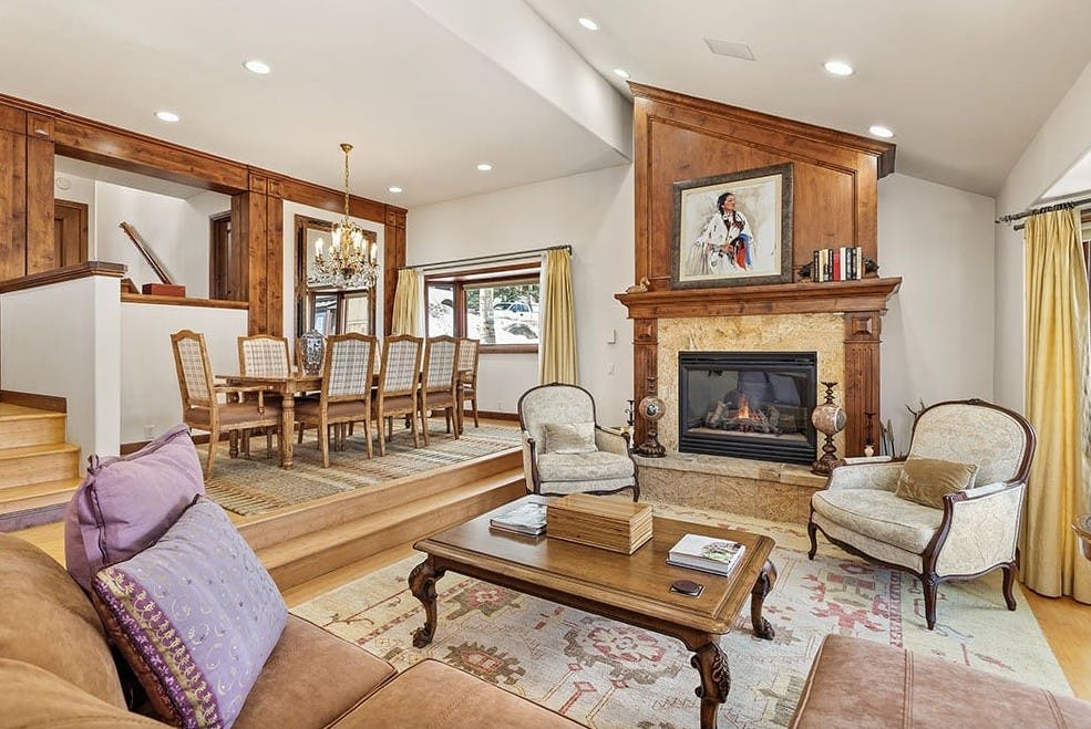 Romantic living room at Residence 13 at Woodrun V Snowmass with antique chairs, dining room table, roaring fireplace, chandelier, and classic dining room table
