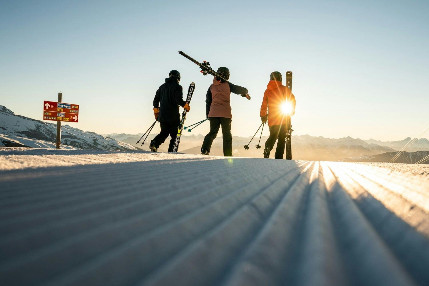Three skiers watch the sunrise over the mountains standing on freshly groomed snow at LAAX