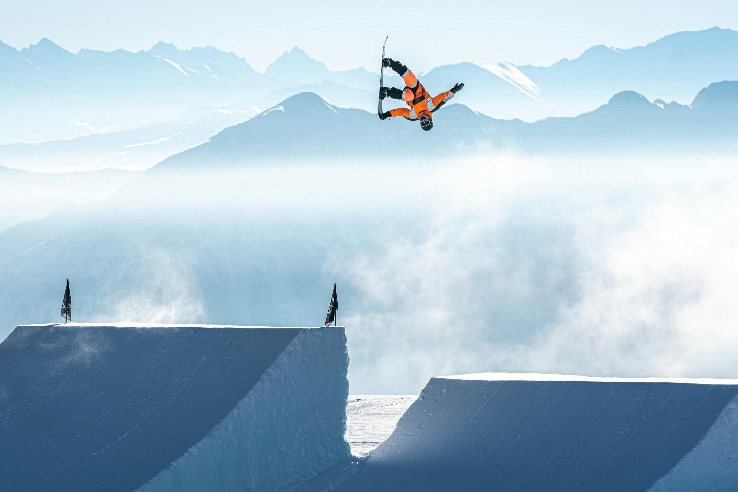 Snowboarder doing a backflip in the air in front of alpine peaks at LAAX Terrain Park