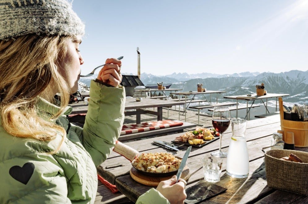 Mom is enjoying a tasty Swiss meal with red wine and alpine views on a sunny deck at LAAX