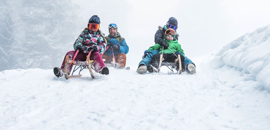 Parents sledding and smiling with their two kids in LAAX Switzerland