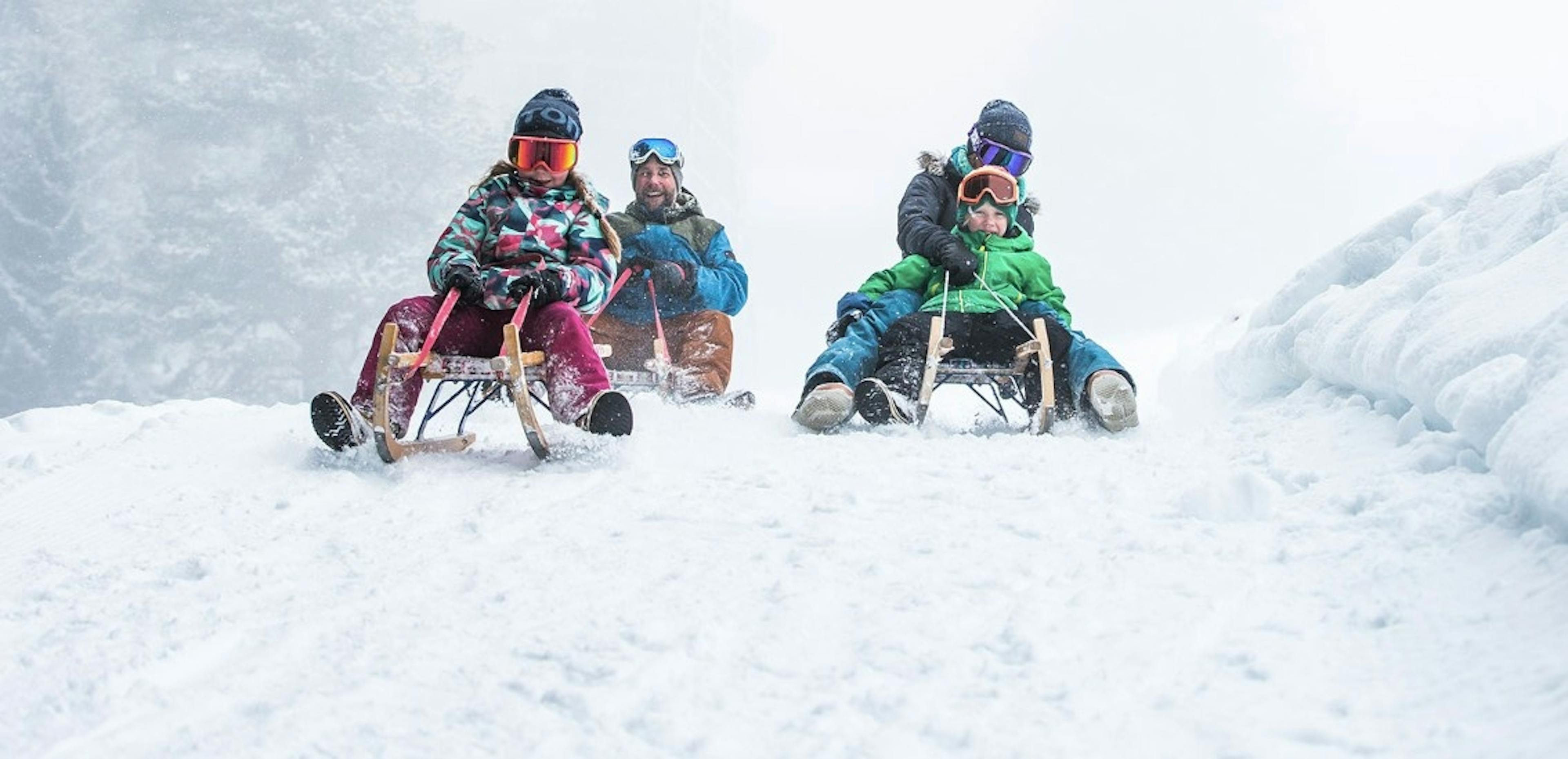 Parents sledding and smiling with their two kids in LAAX Switzerland