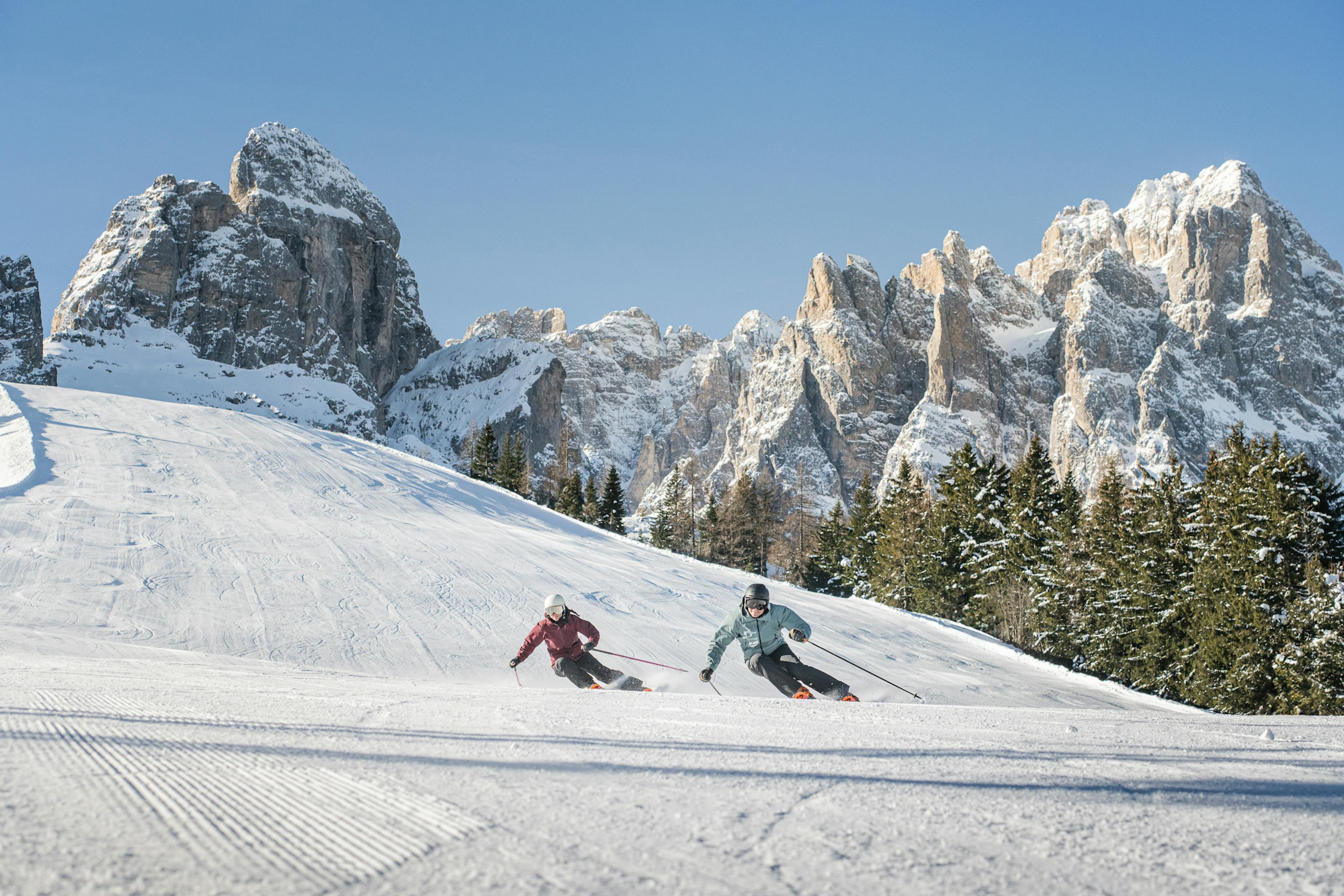 Two skiers of undiscernible gender in colorful ski attire hitting the slopes at Three Peaks (3 Zinnen Dolomites) in Italy, Europe.