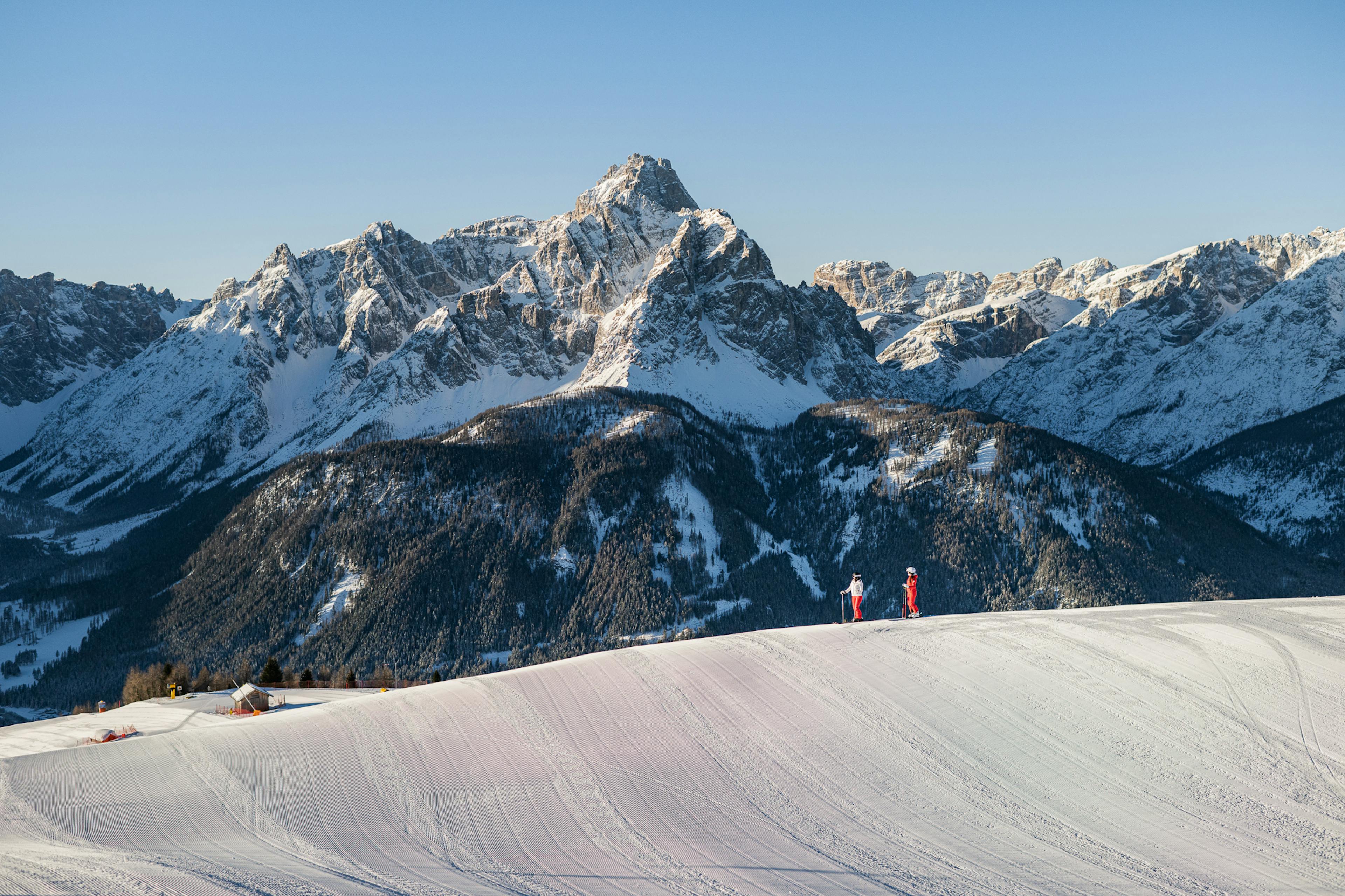 Two skiers of undiscernible gender in pink and white ski attire gazing at the peaks on a winter afternoon at Three Peaks (3 Zinnen Dolomites) in Italy, Europe.