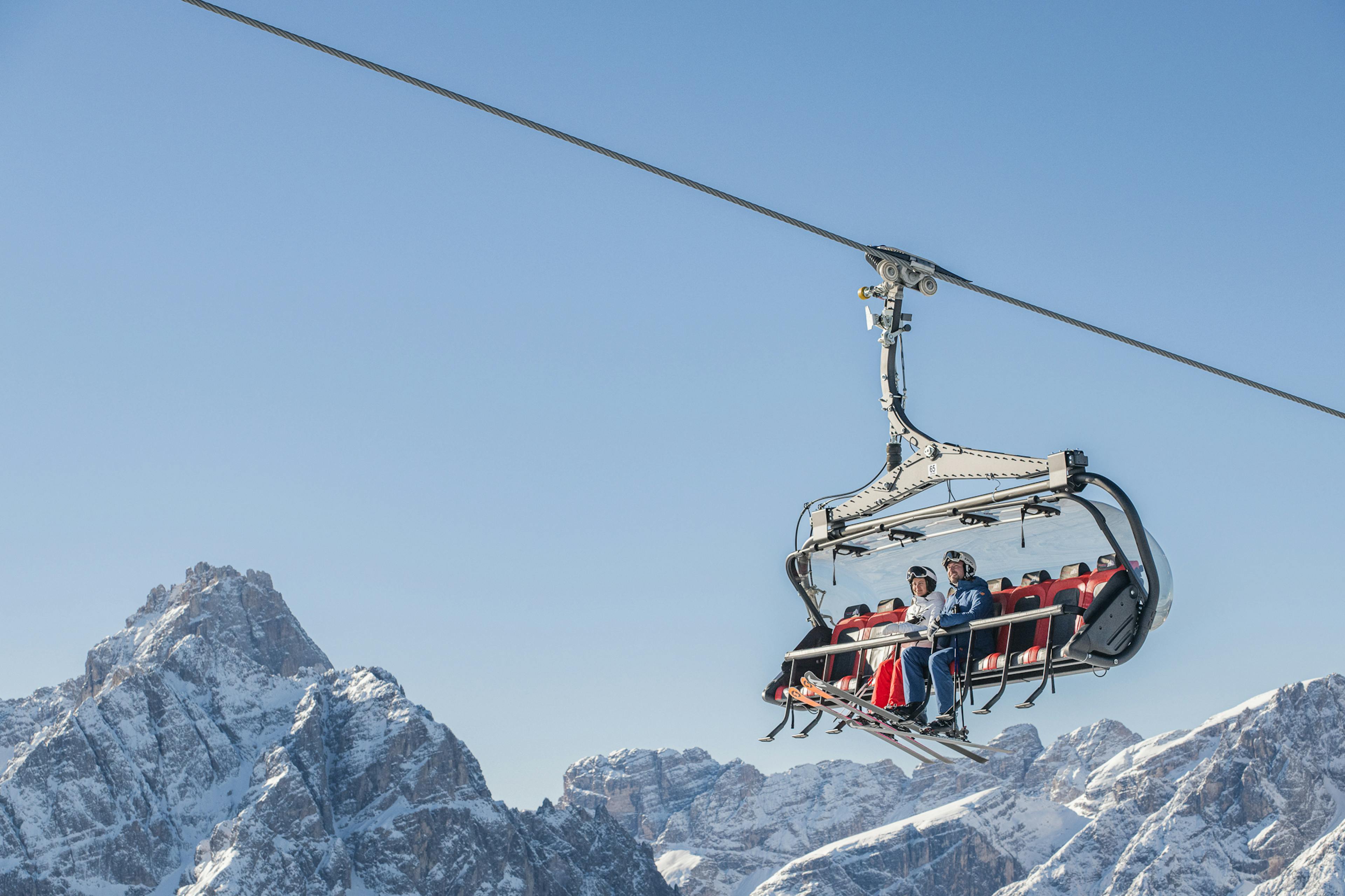 Male and female skier in colorful ski attire riding the chairlift up the slopes at Three Peaks (3 Zinnen Dolomites) in Italy, Europe.
