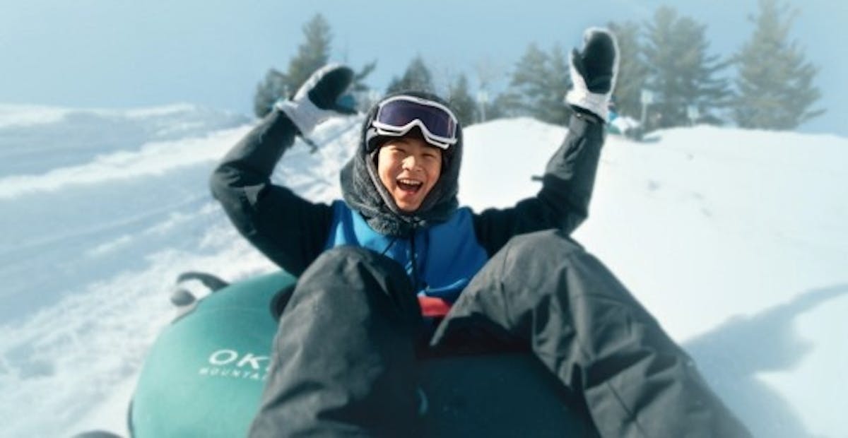 A teenager laughing with their hands in the air while snow tubing at Okemo Resort
