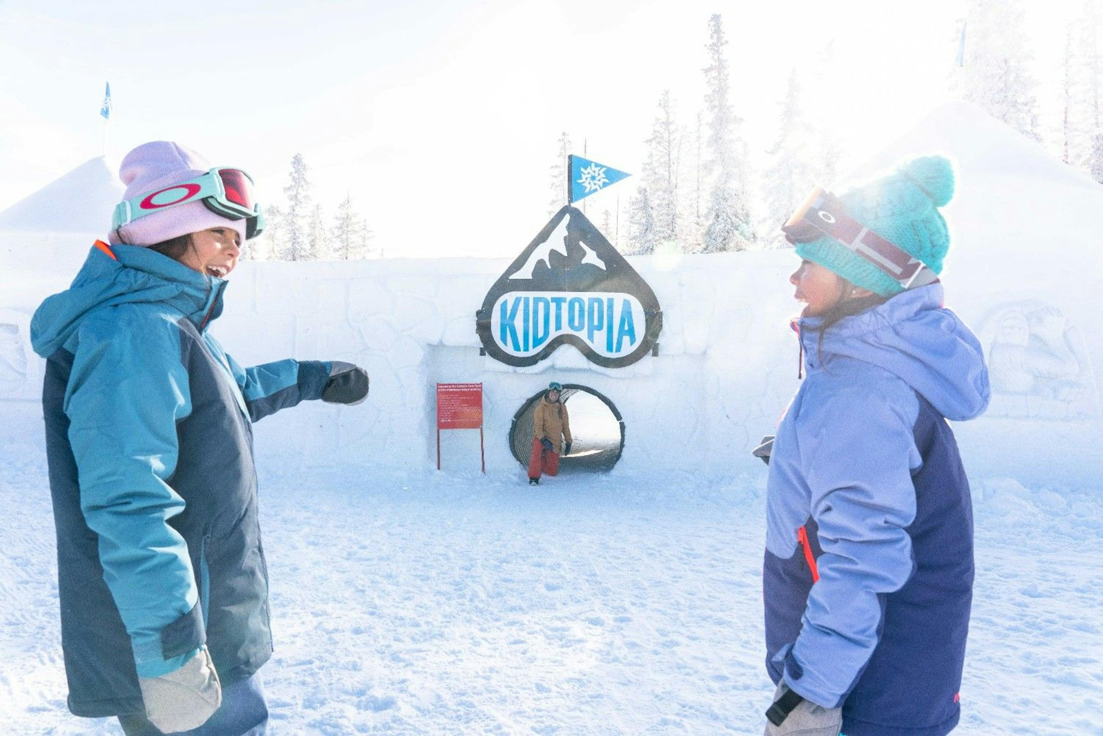 Two kids in ski gear stand smiling and laughing in front of Kidtopia at Keystone