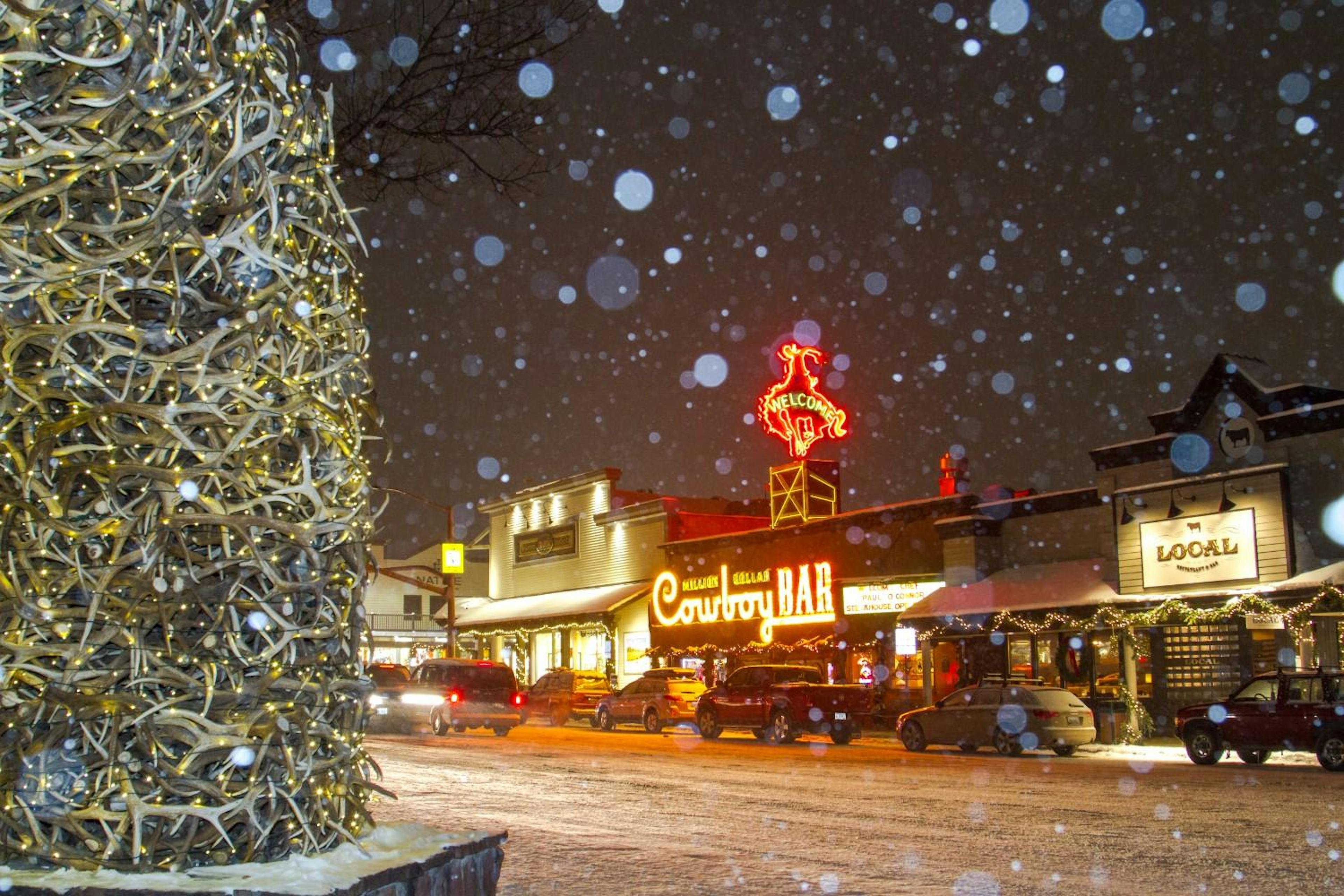 Snowy street at night in the town of Jackson with the Cowboy Bar and Jackson Hole’s Elk Antler Arch in view