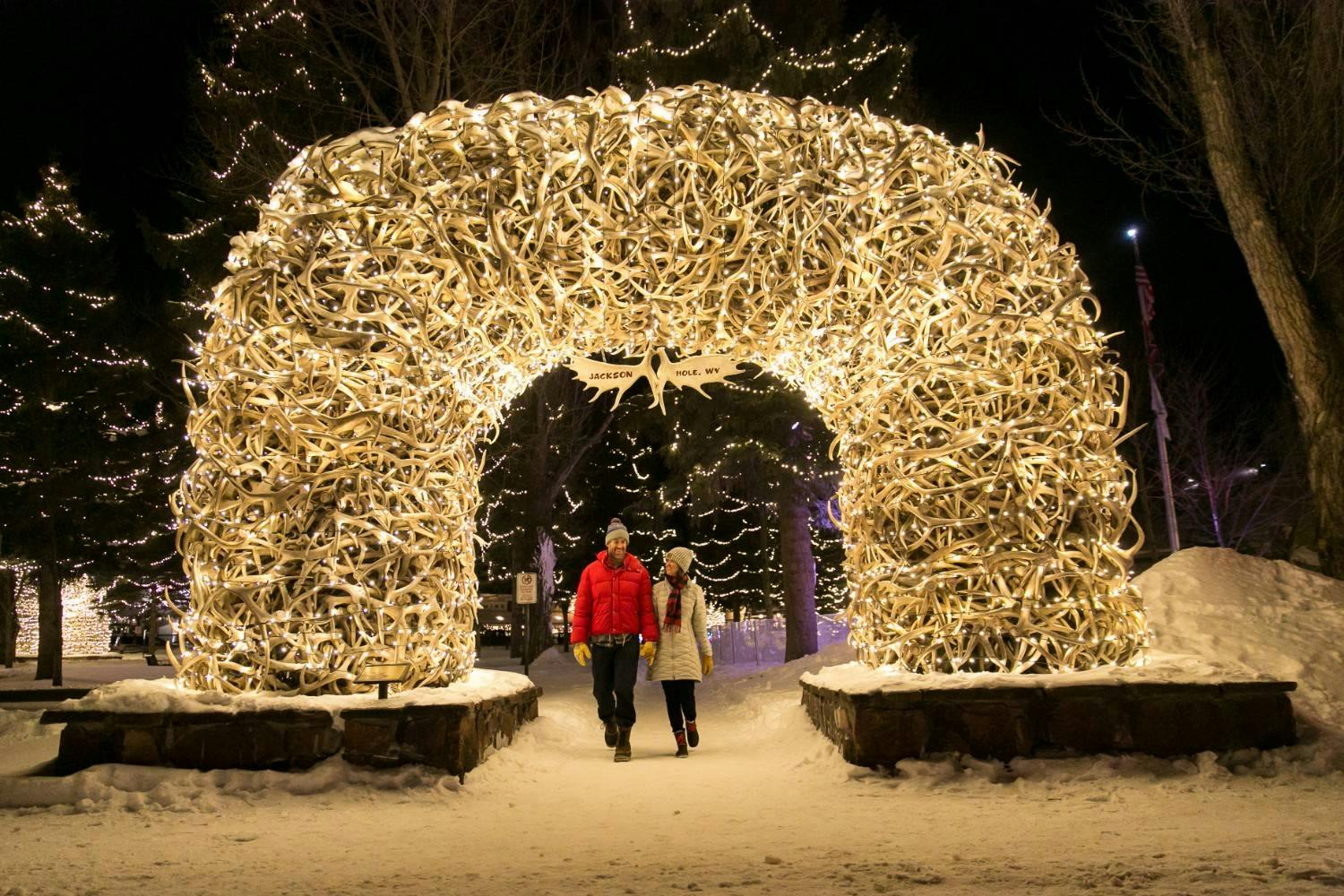 A couple walks under Jackson Hole’s Elk Antler Arch covered in lights at night