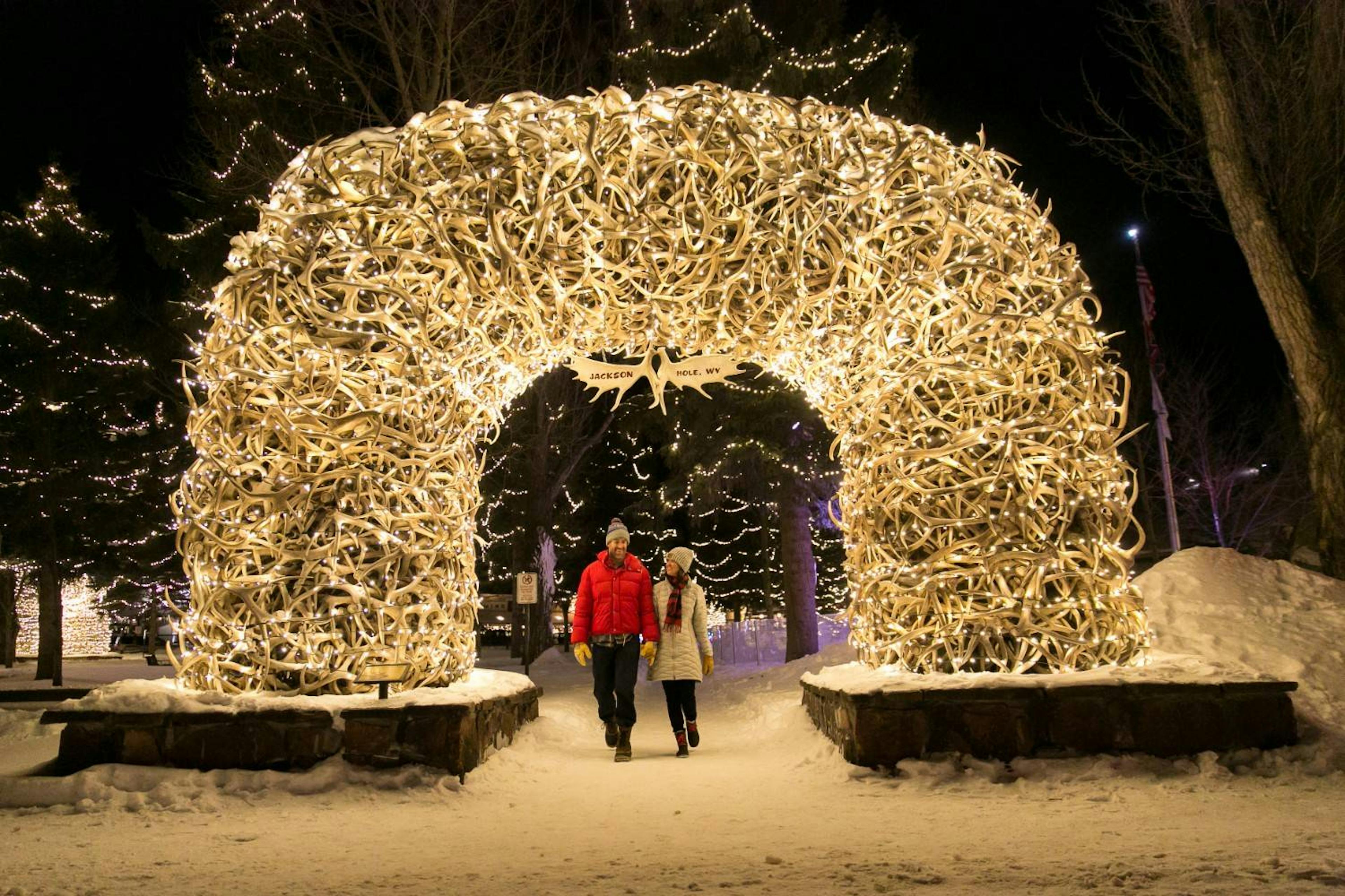 A couple walks under Jackson Hole’s Elk Antler Arch covered in lights at night