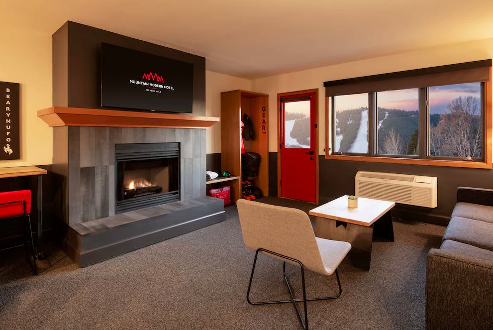 Living room inside Mountain Modern Jackson Hole with a roaring fireplace, table, couch, gear storage and beautiful view of the sunset over the slopes of Jackson Hole Resort