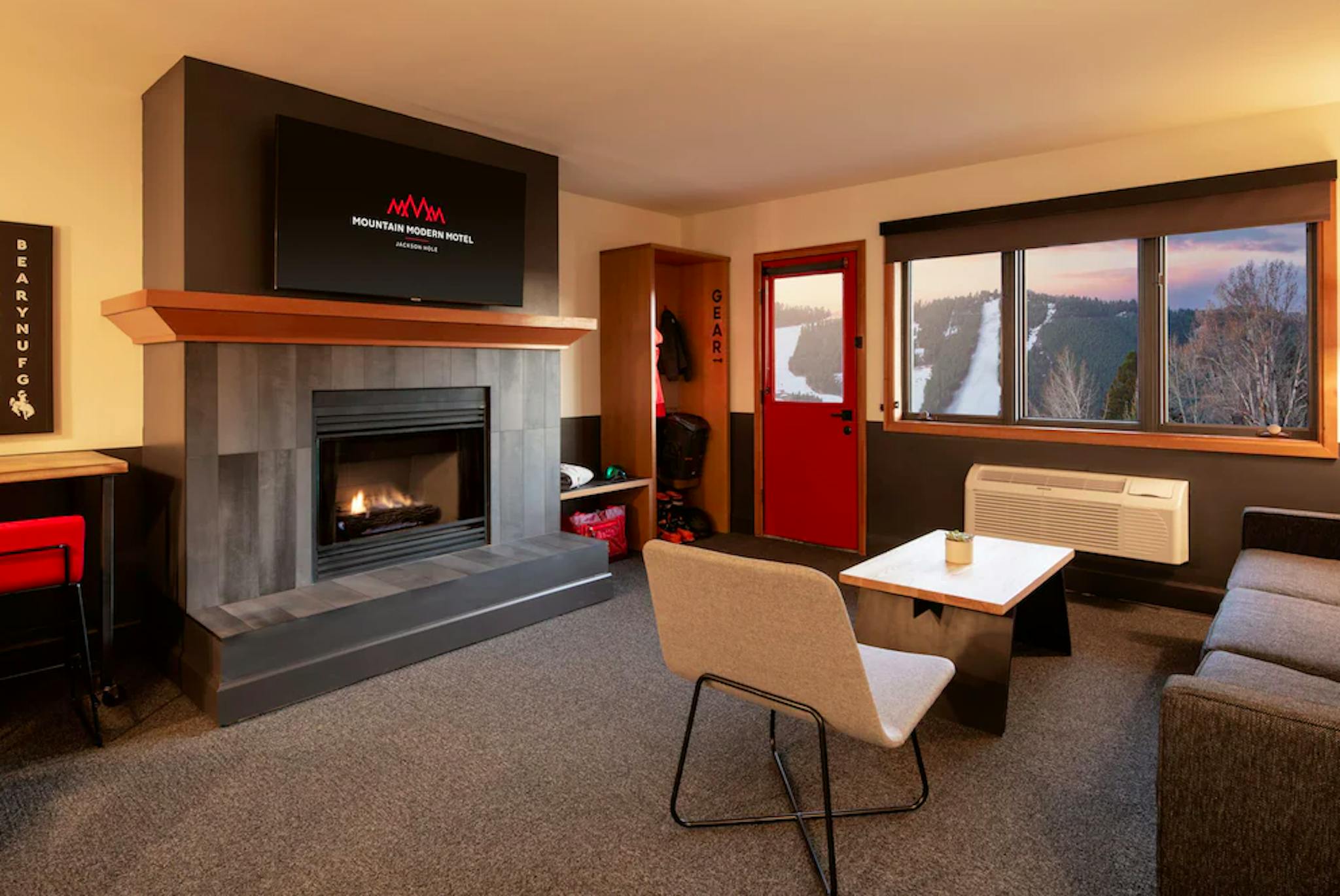 Living room inside Mountain Modern Jackson Hole with a roaring fireplace, table, couch, gear storage and beautiful view of the sunset over the slopes of Jackson Hole Resort