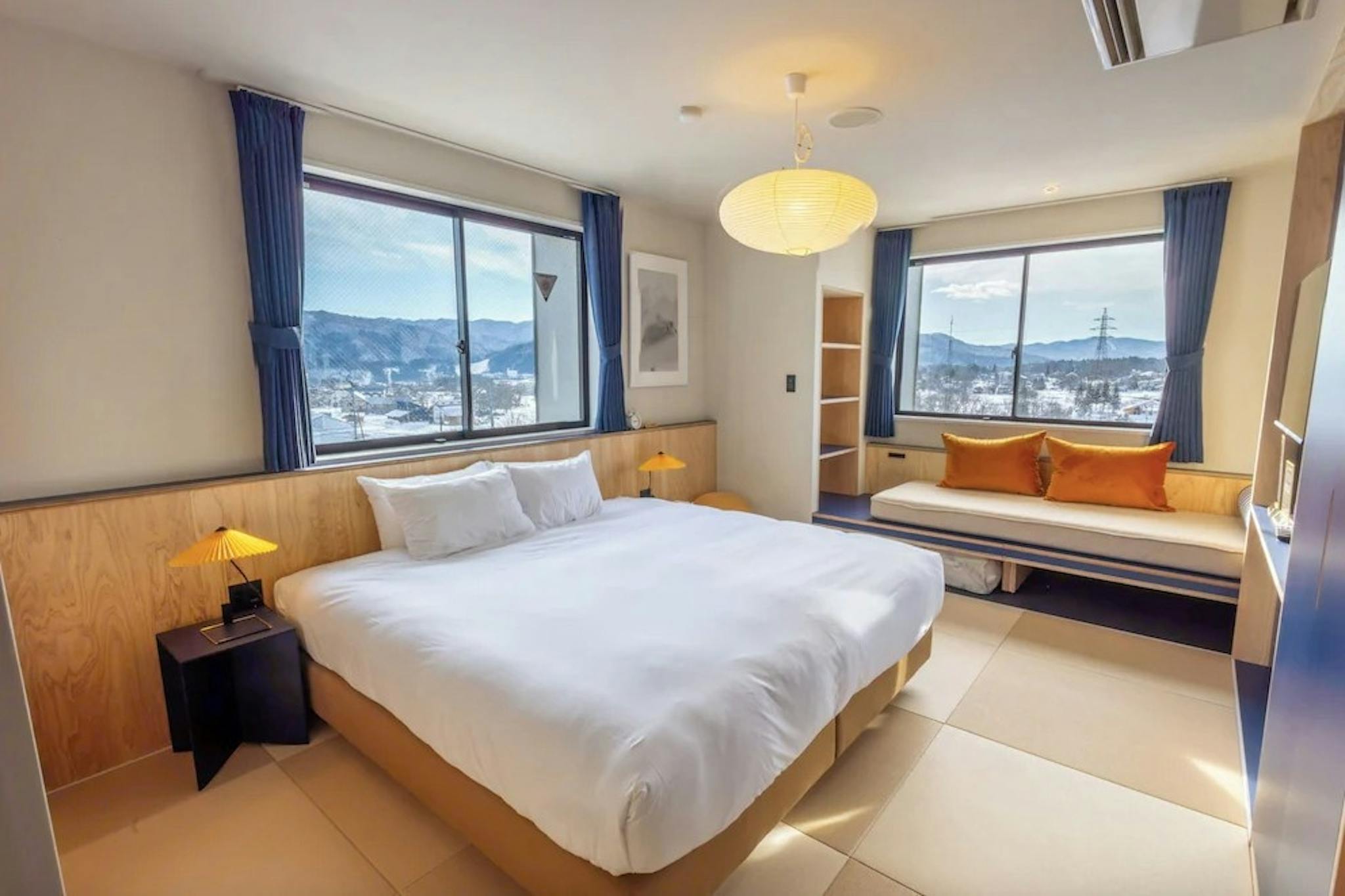 A hotel room in Evo Hotel Hakuba with a huge king bed with white comforter, modern couch, and views of the ski slopes from the bedroom window