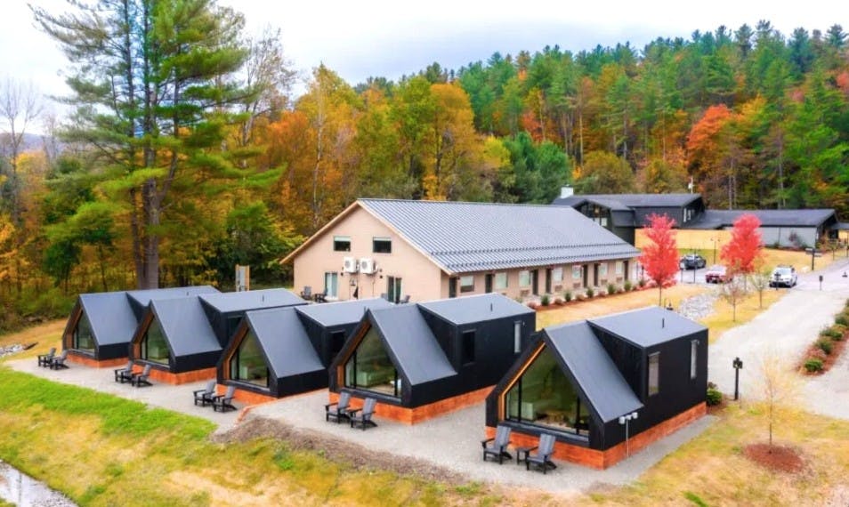 Collection of A-frame cabins at Outbound Stowe framed by trees with autumn leaves