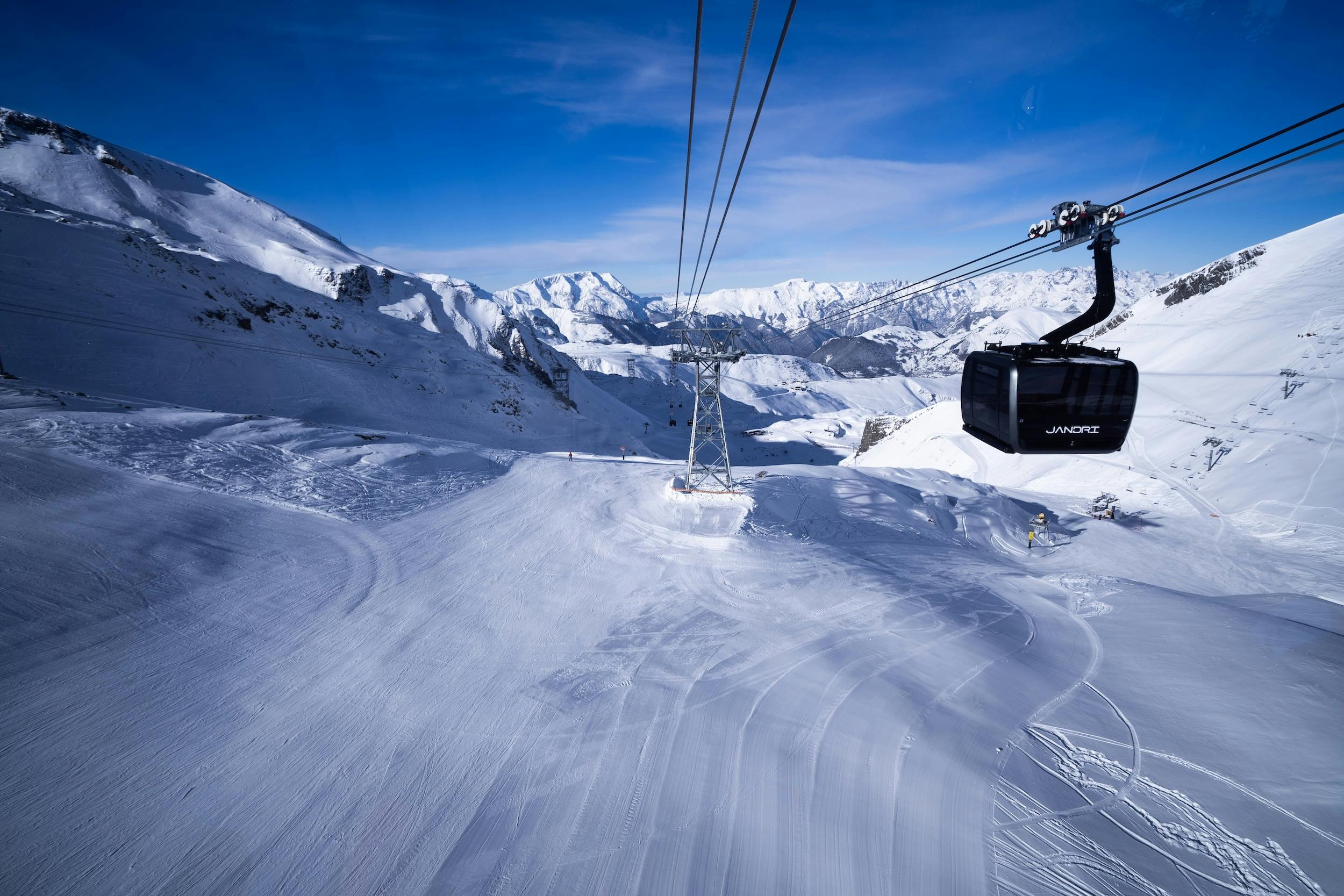 A ski gondola ascending through a snowy landscape under a clear blue sky.