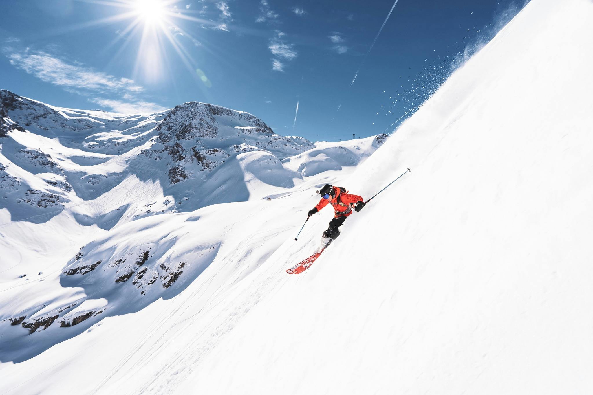 A person skis down a slope, with a panoramic view of the mountain range behind them.