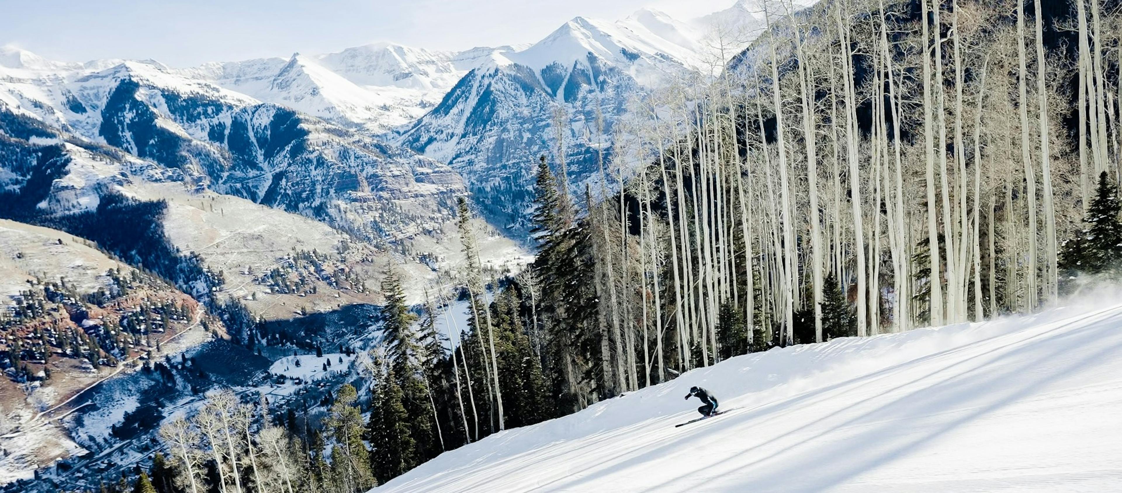 A skier descends a mountain slope in Telluride, surrounded by tall trees in the background