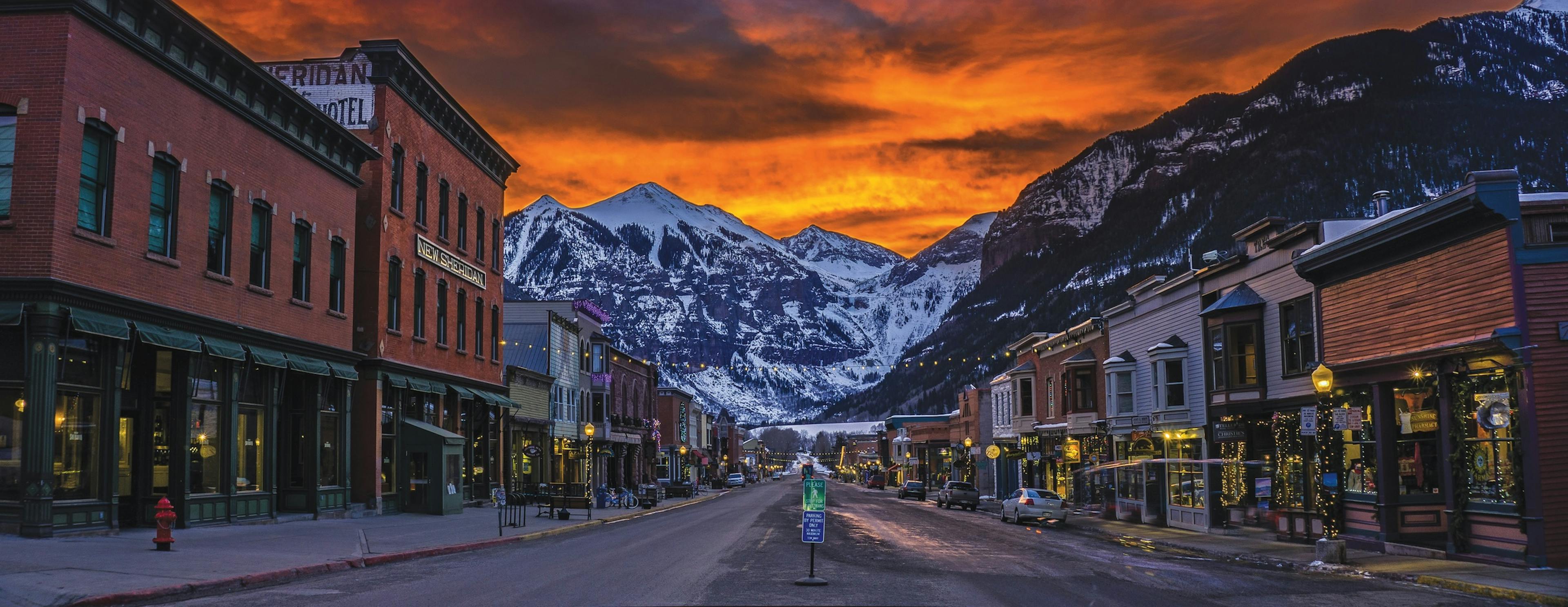  A city street in Telluride with majestic mountains rising in the background under a clear blue sky.