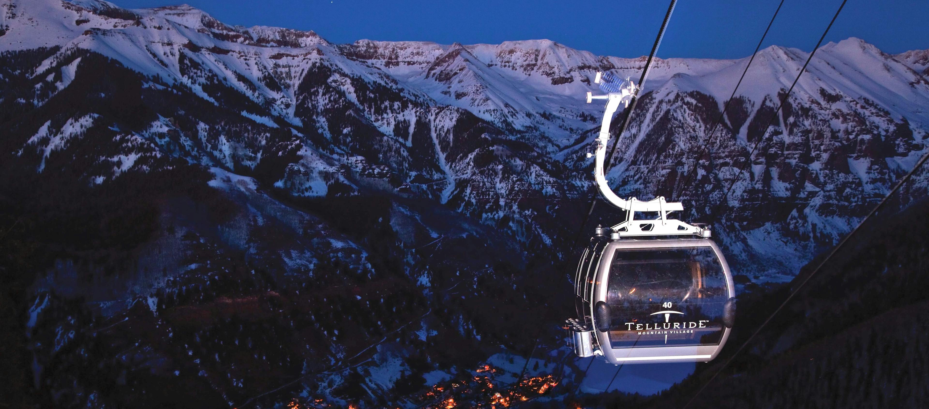 A gondola ride in the mountains of Telluride at dusk, with a colorful sky and silhouettes of peaks in the background.