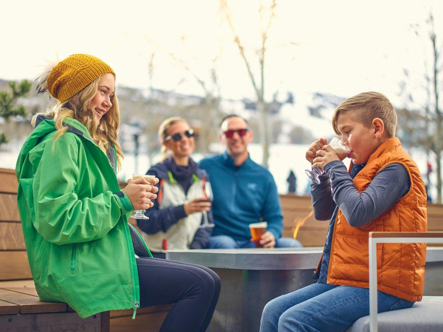 A family sits outside sipping hot chocolate at Snowmass' Electric Pass Lodge.
