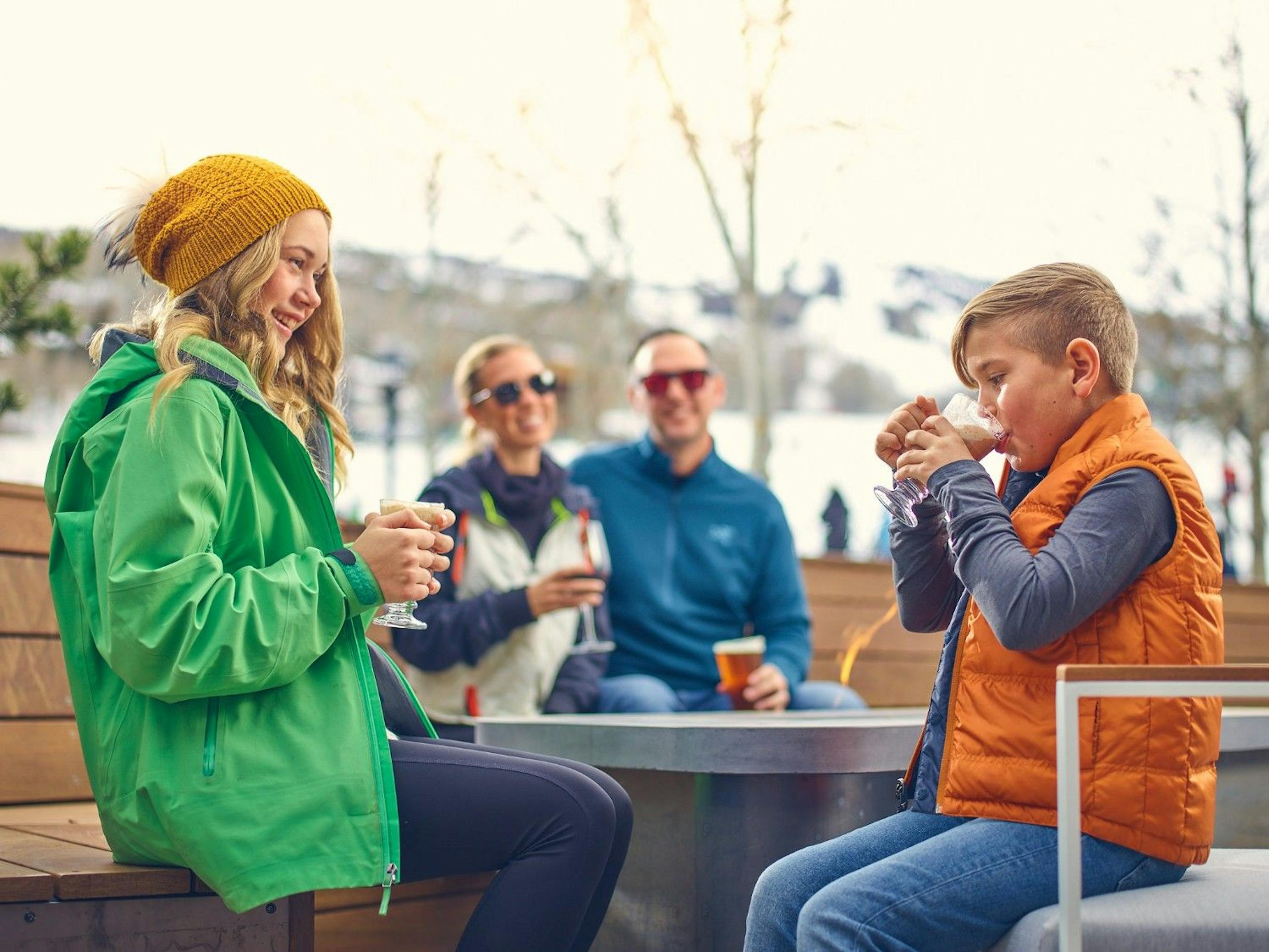 A family sits outside sipping hot chocolate at Snowmass' Electric Pass Lodge.