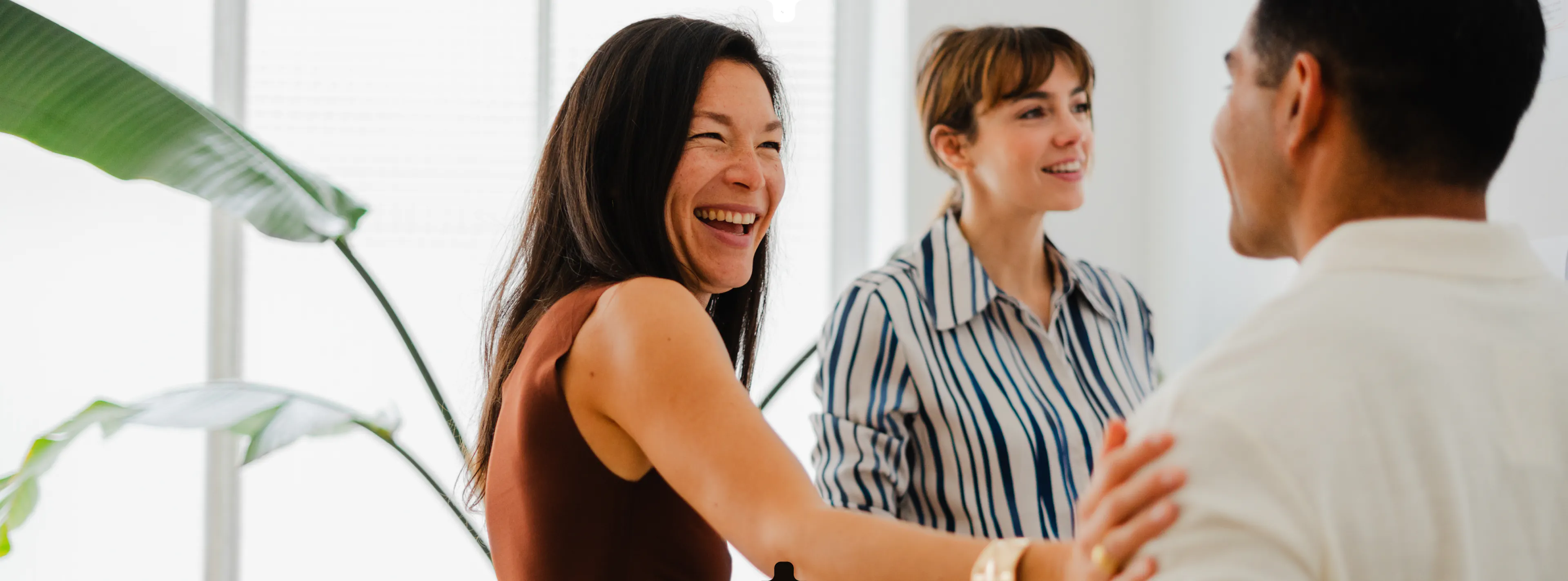 Trois collaborateurs échangent en souriant dans un bureau