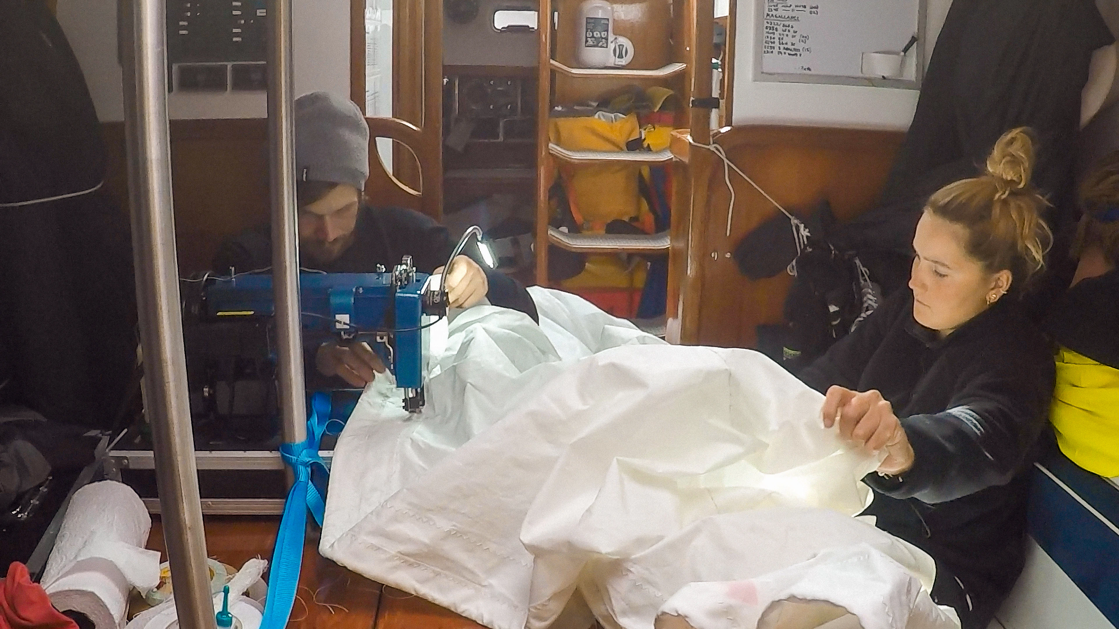 A man and a woman fixing a broken sail inside a sailing boat.