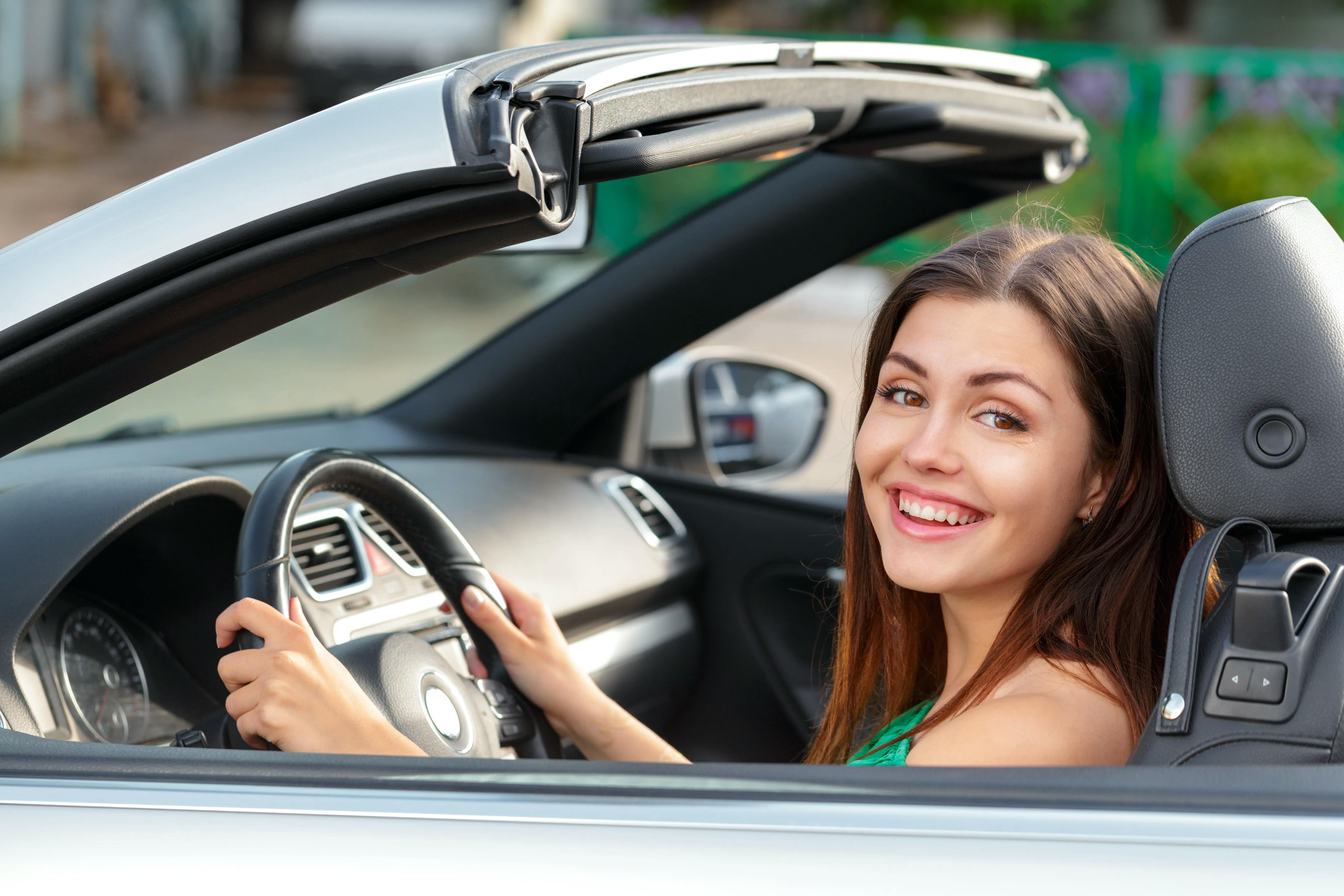 A young woman smiling in a convertable car with the roof open.
