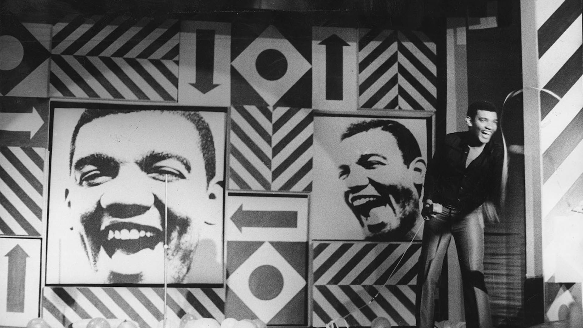 Simonal, em foto preto e branco, se apresenta num palco com grafismos geométricos, linhas diagonais, setas, losangos e círculos, e fotos do seu rosto em alto contraste, dispostas em uma composição assimétrica