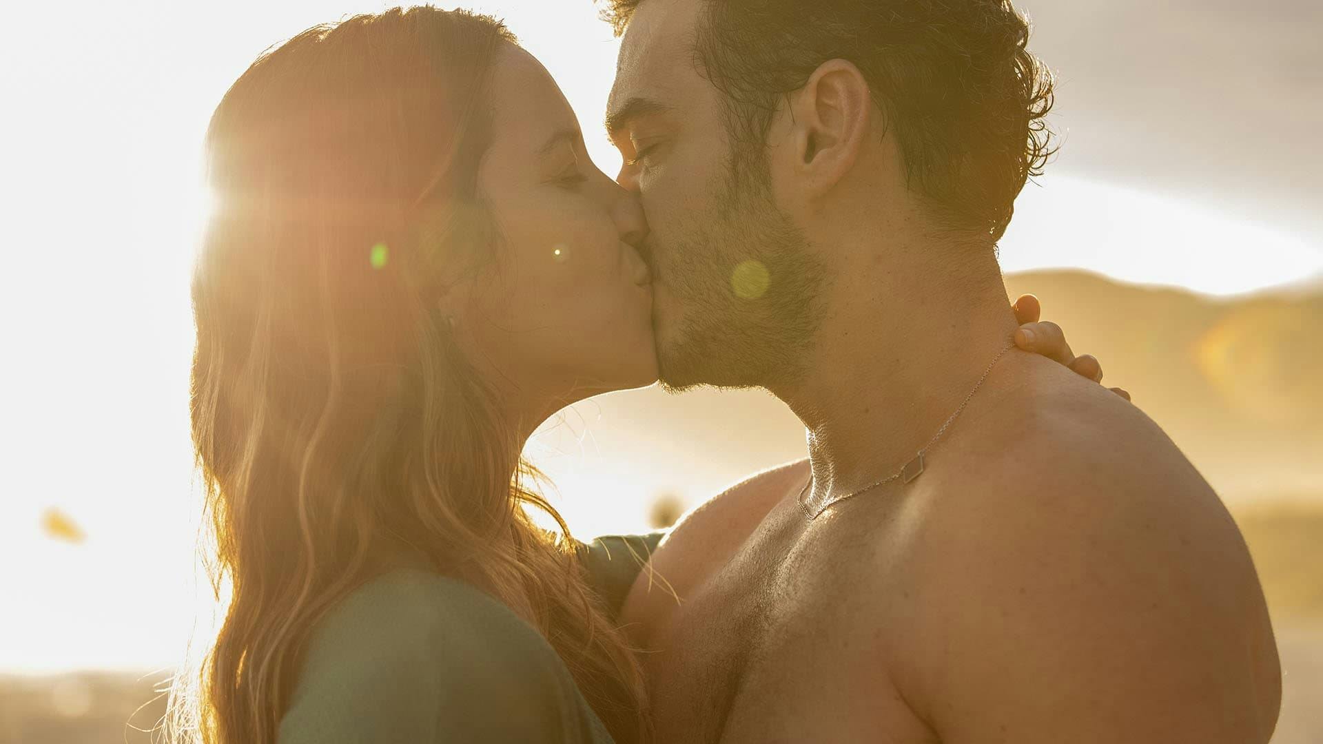 um casal, formado por um homem e uma mulher, se beijando num por do sol
