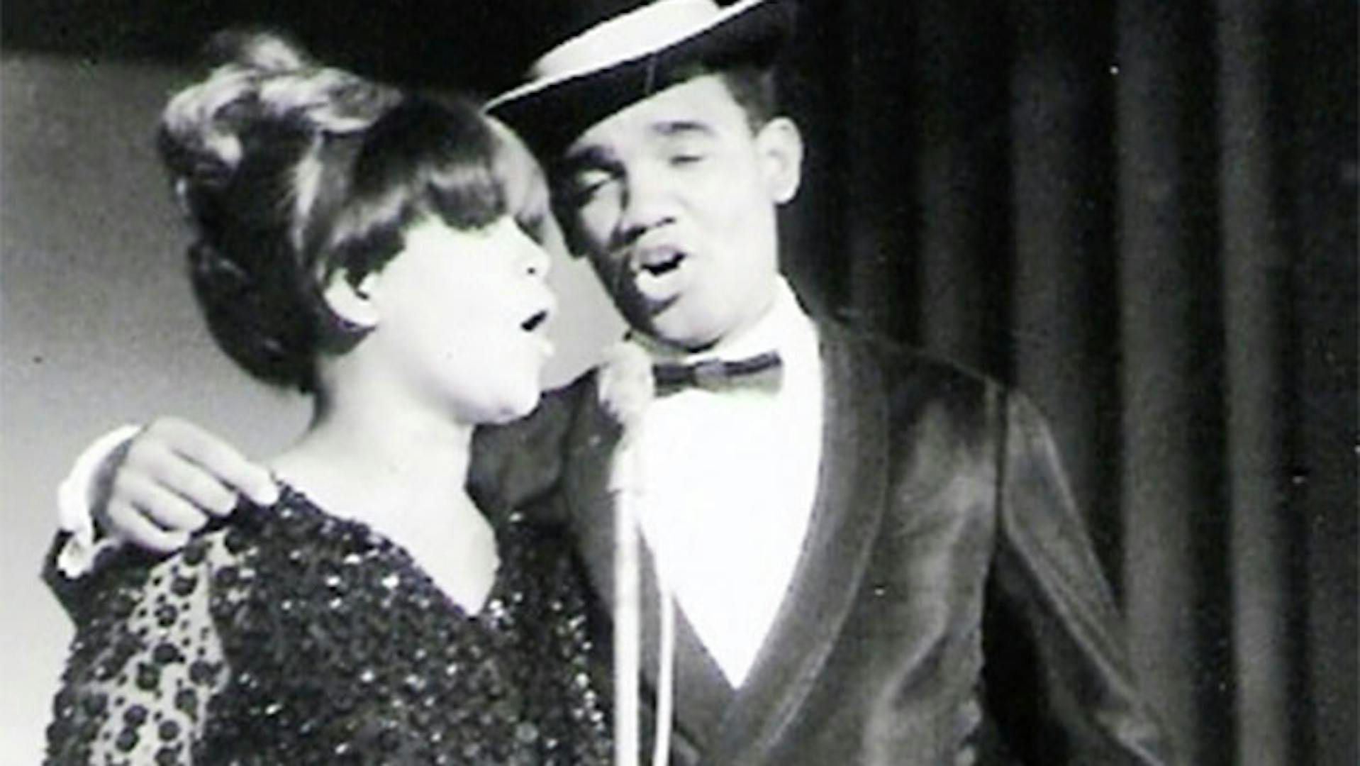 Simonal se apresentado em uma foto, preto e branca, ao lado de uma cantora