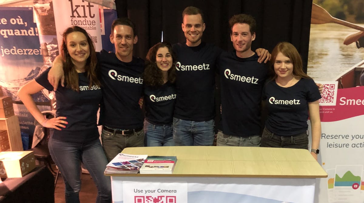 Les membres de l'équipe Smeetz s'étreignent et sourient en portant des T-shirts Smeetz à Adventure Expo.