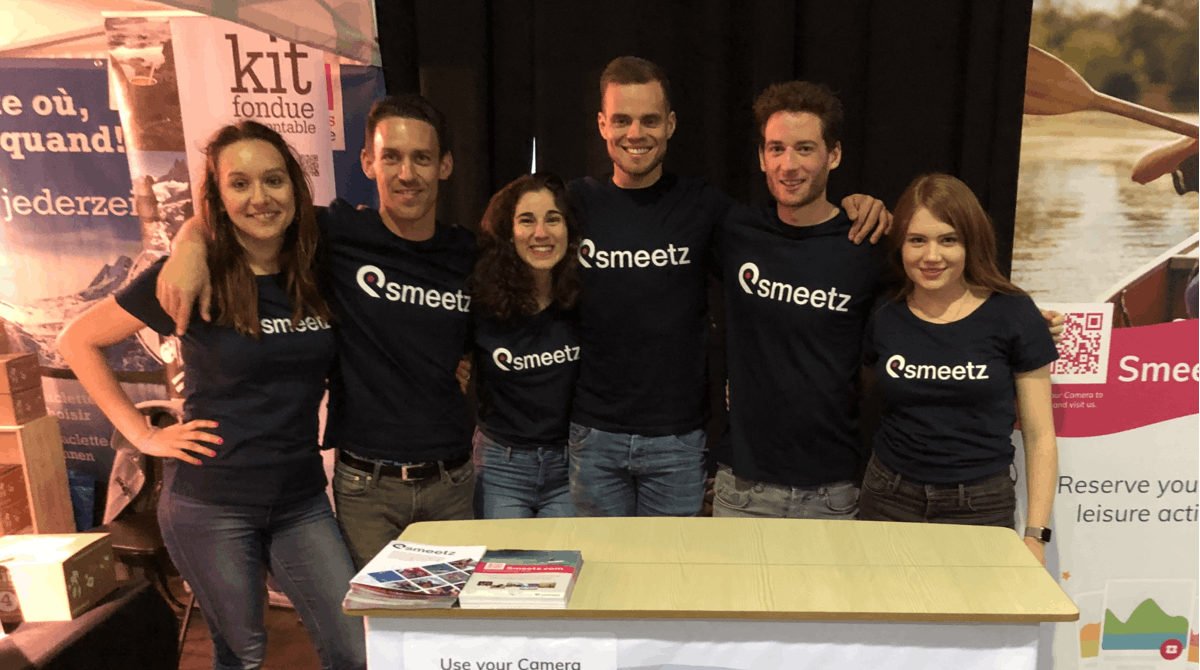 Smeetz team members hugging and smiling wearing Smeetz T-shirts at Adventure Expo.
