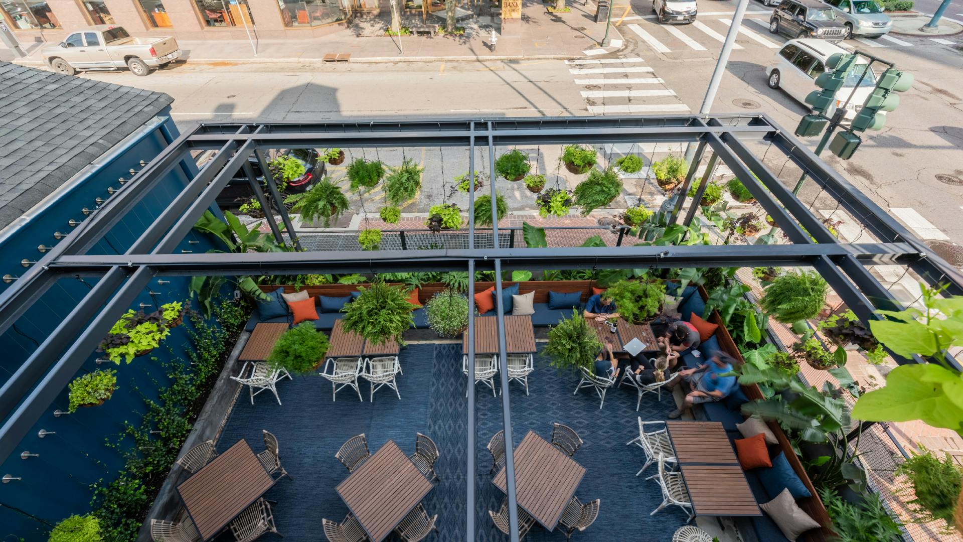 bird's eye view of the courtyard, table tops with lush tropical planting along the perimeter and hanging baskets above steel structure.
