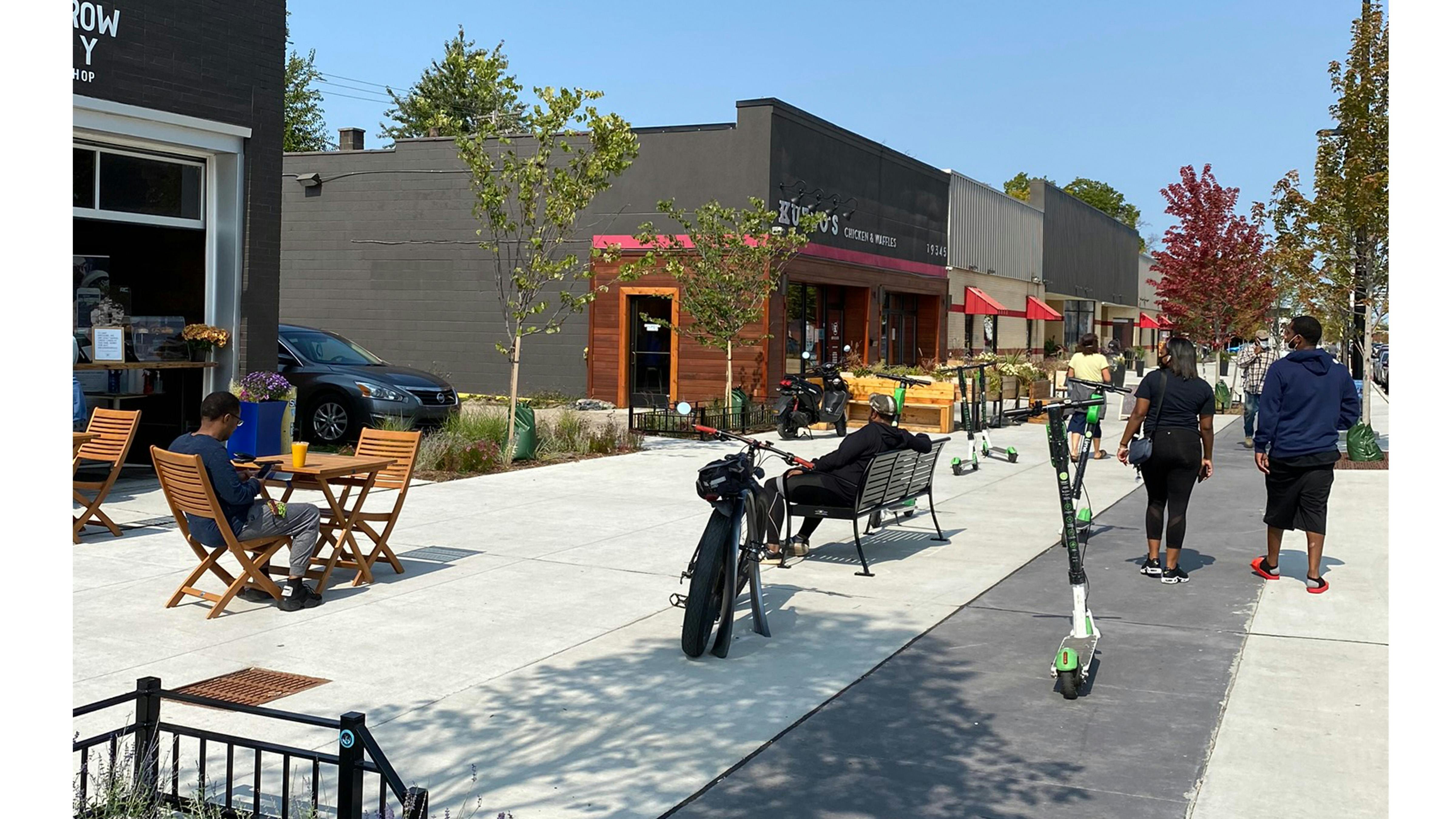 Installed photograph of bike lane separating roadway and pedestrian sidewalk with variety of outdoor storefront seating.