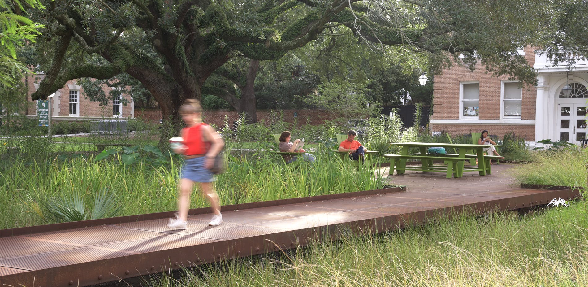 Student walks through garden with other students reading in the background.