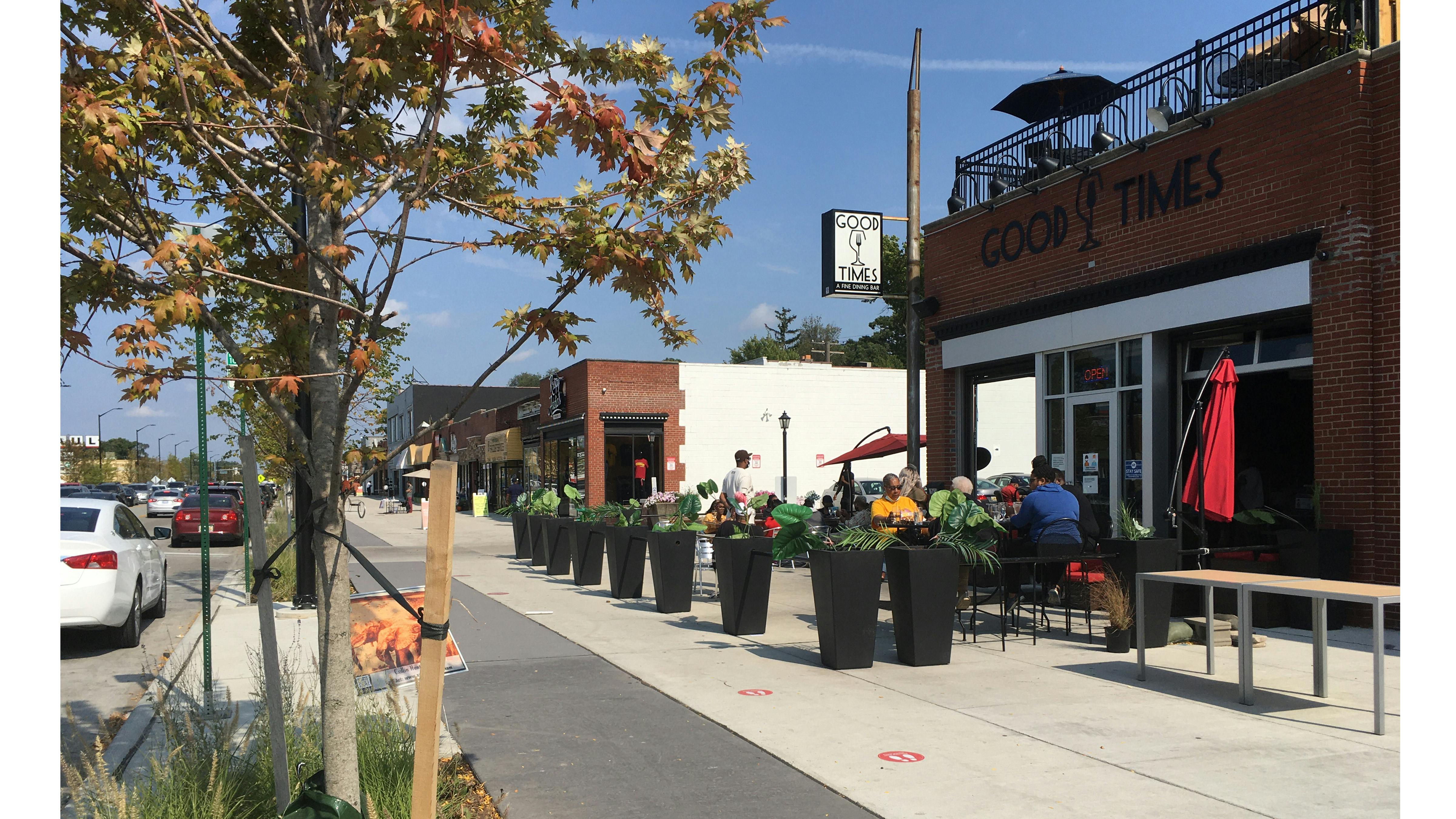 Installed photograph of bike lane and roadway separated by planting beds and trees, bike lane and storefront separated by outdoor seating and planters.