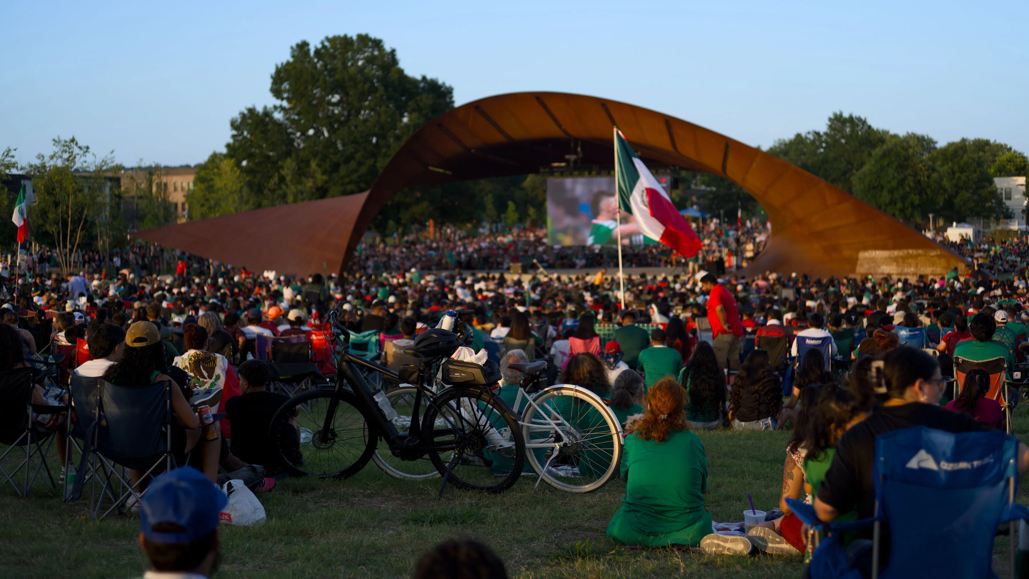 crowd sitting in park watching Mexico soccer game on big screen
