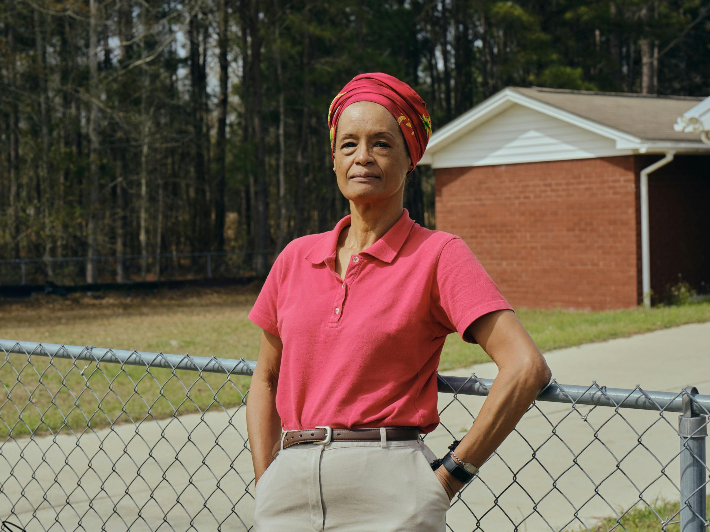 Woman stands in front of a chain fence and her home