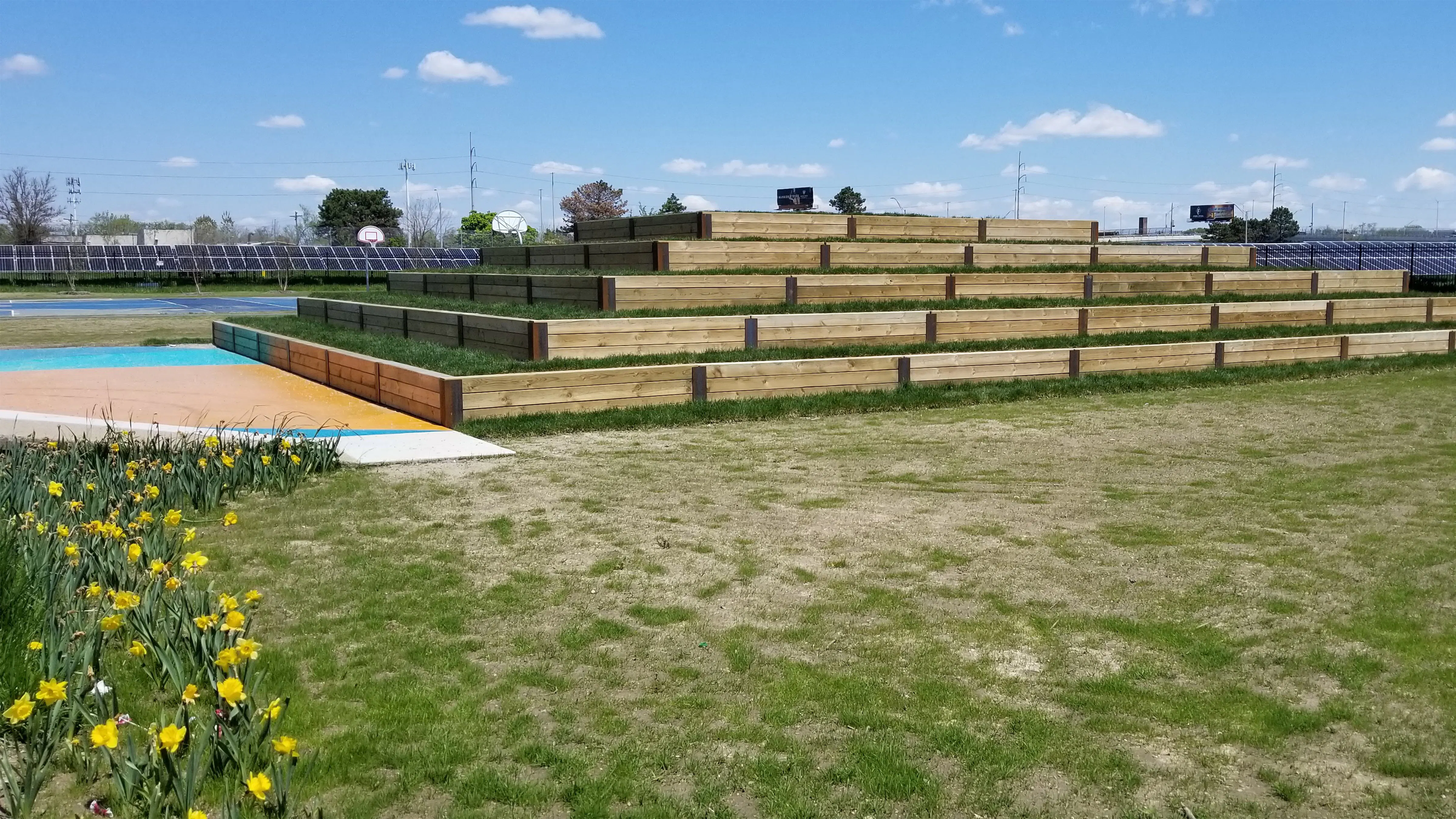 Wooden tiered terraces nearby play courts and a flowerbed in the foreground