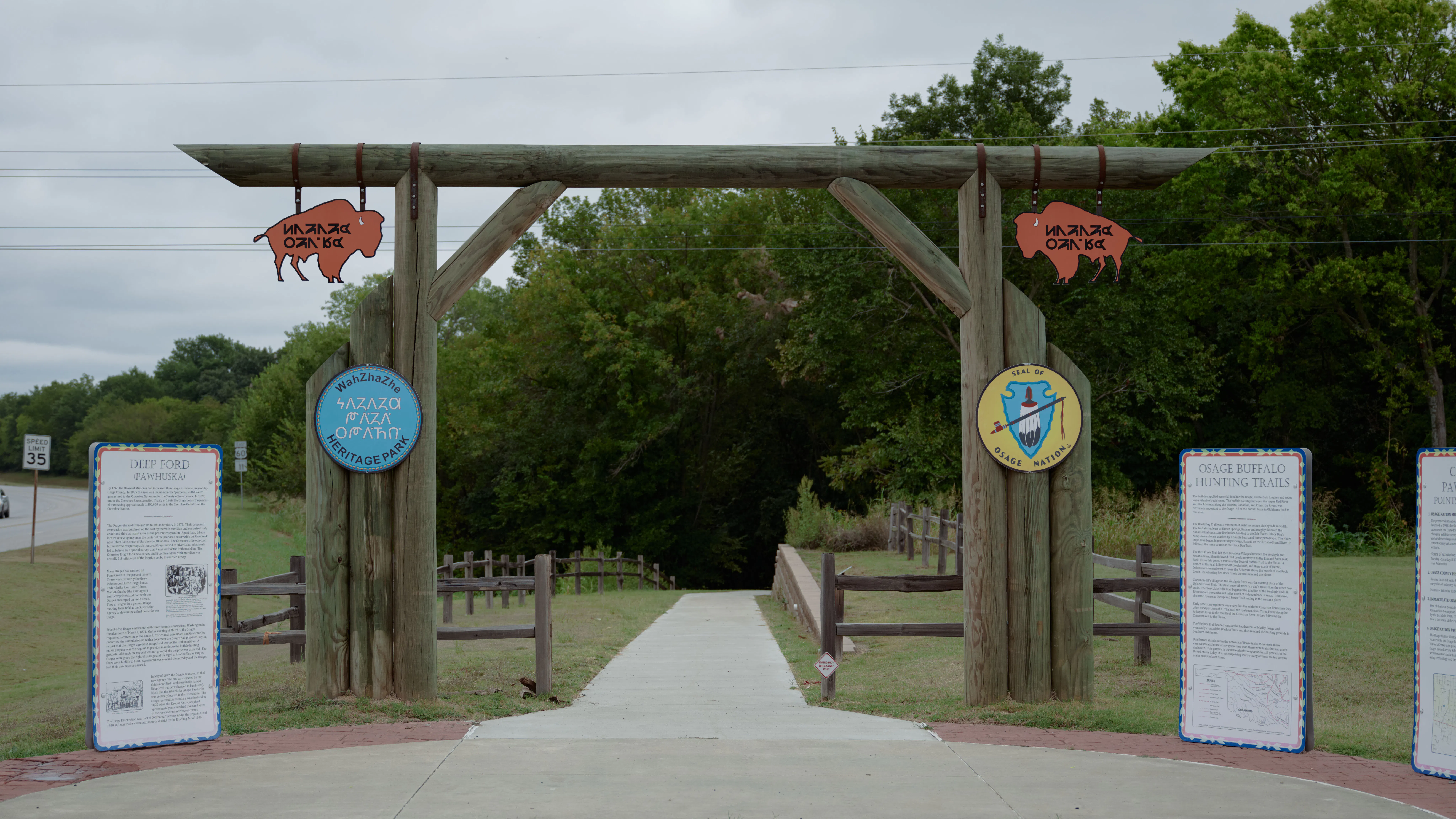 Wooden structure entrance going towards a pedestrian path with nearby wayfinding sign flanking the entrance