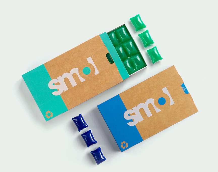 un pack de capsules de lessive active marron et vert donc le tiroir est ouvert, révélant six capsules de lessive vertes, à côté de trois capsules de lessive alignées à la verticale ; et un pack de capsules de lessive sensitive marron et bleu donc le tiroir est ouvert, révélant six capsules de lessive bleues, à côté de trois capsules de lessive alignées à la verticale.