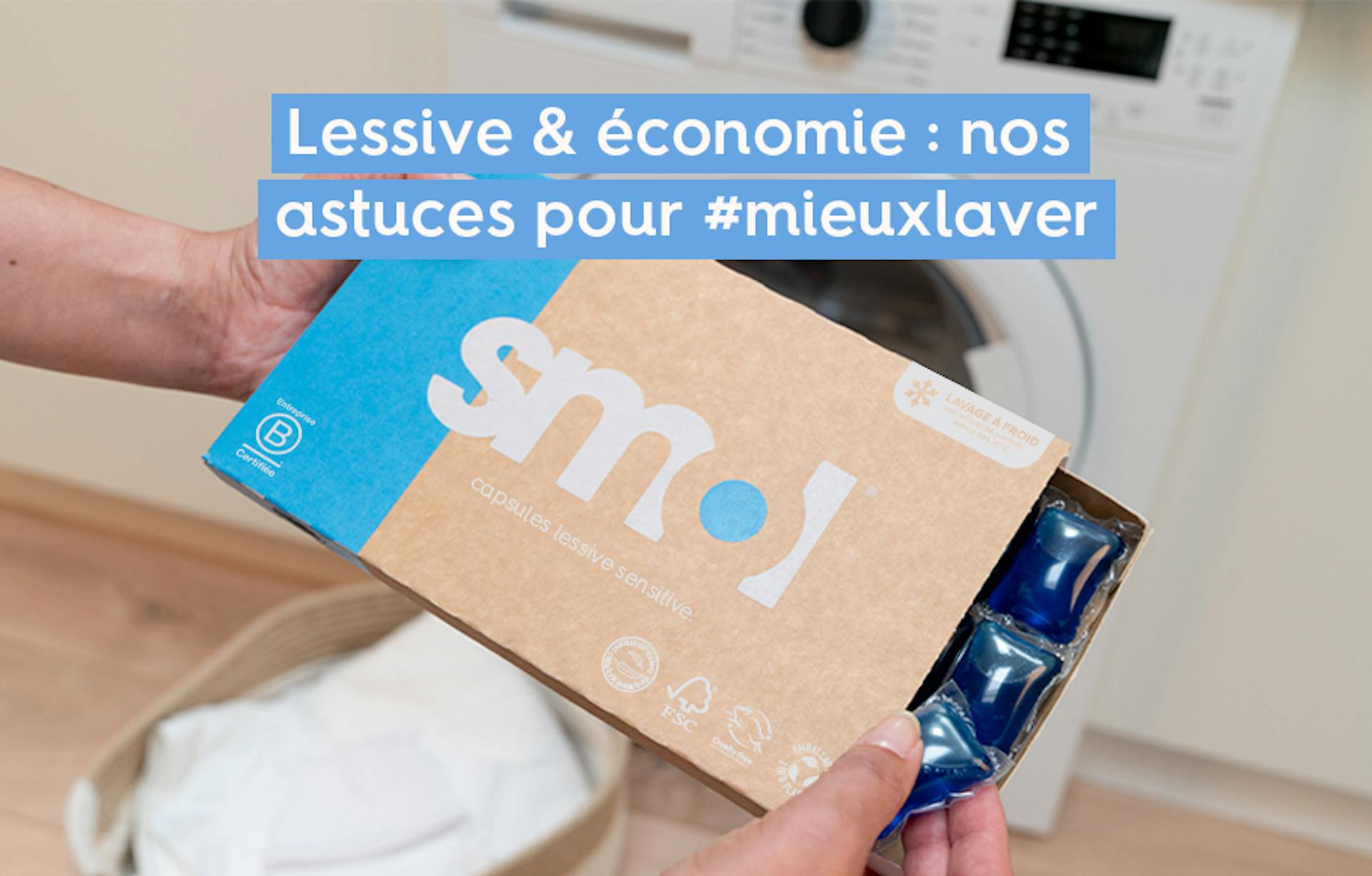 pack de capsules lessive sensitive smol tenu par quelqu'un, dont le tiroir est ouvert, devant une machine à laver.