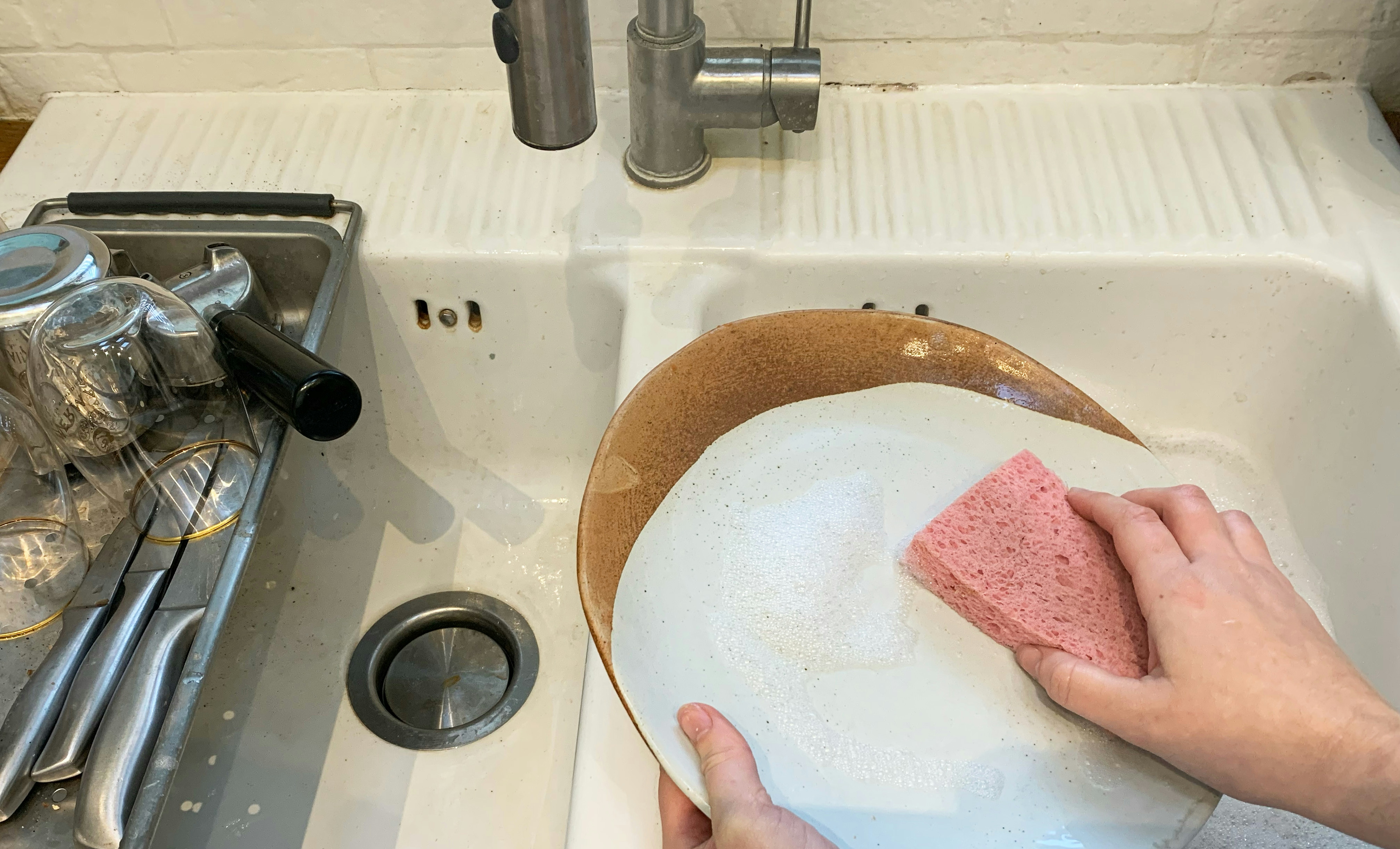 mains lavent une assiette sale avec une éponge rose au-dessus d'un évier