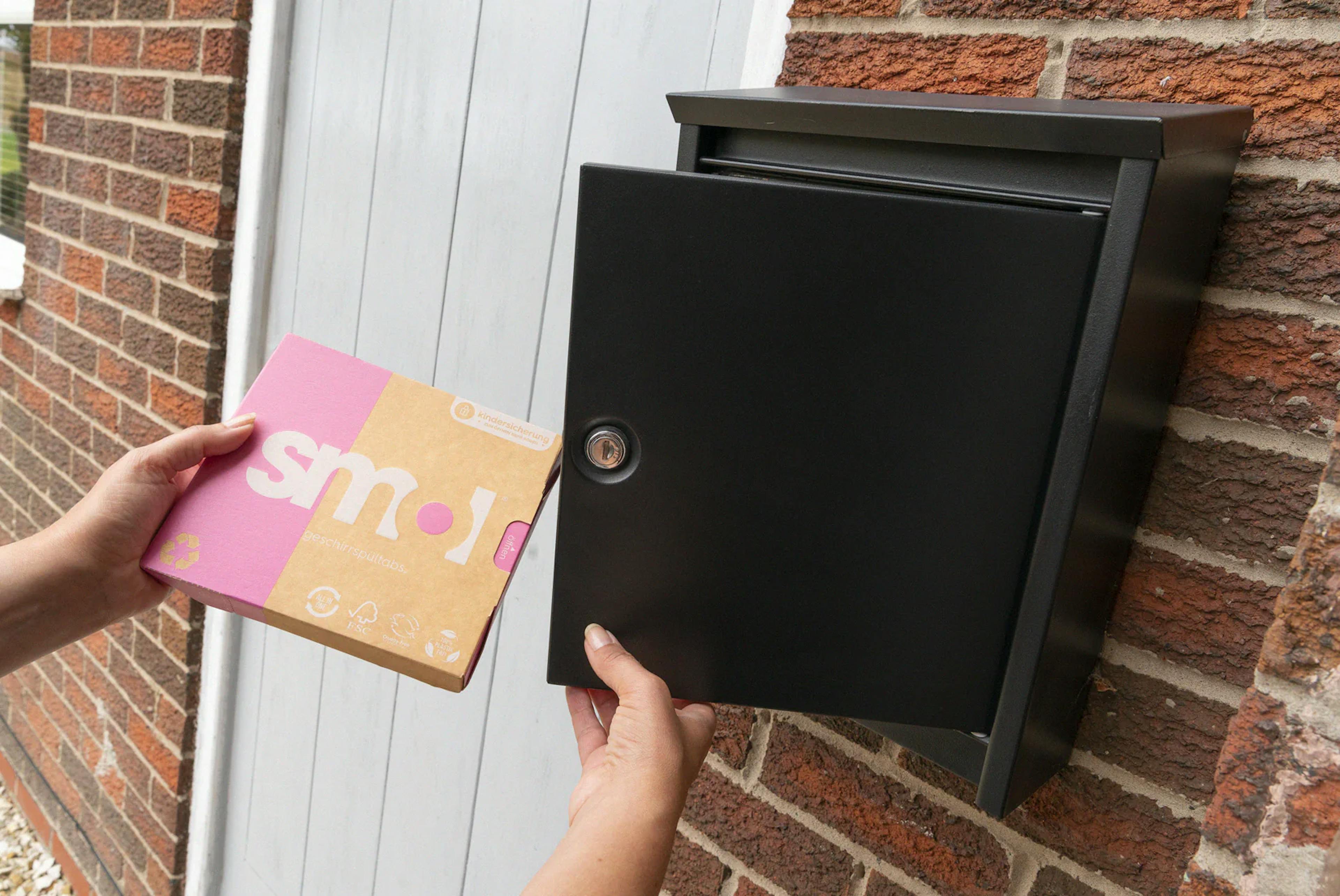 eine Packung smol Geschirrspültabs, die aus einem außen am Haus angebrachten Briefkasten entnommen wird