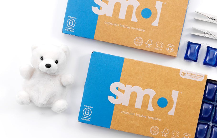 deux packs de capsules lessive sensitive posés l'un à côté de l'autre avec le tiroir ouvert et quelques capsules dehors, et deux ours blancs en peluche.